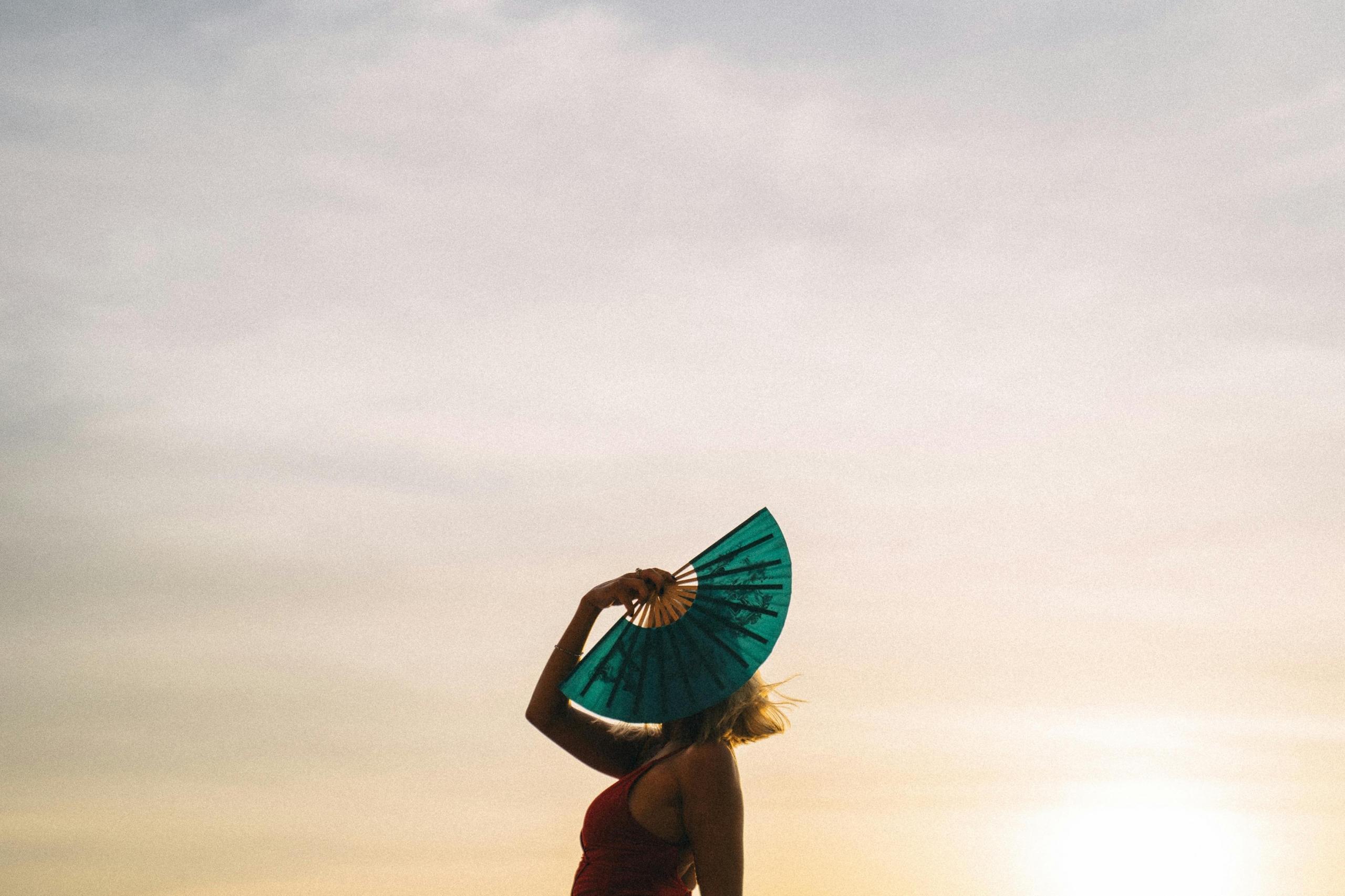 dancer in red dress hiding face with paper fan outdoors at sunset