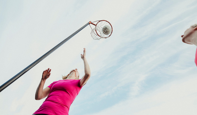women in fuchsia tops playing netball and goal shooter throwing ball into net