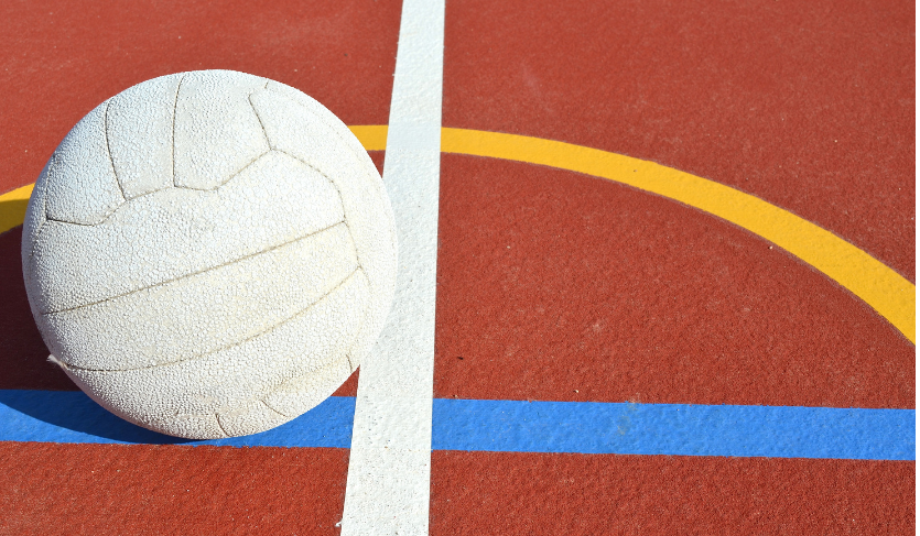 white netball placed in centre of outdoor netball court with yellow and blue markings