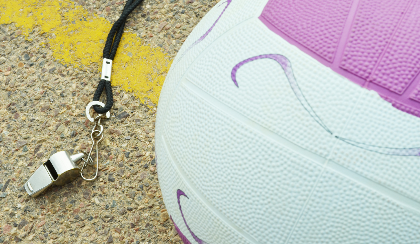 whistle and netball placed side-by-side on netball court