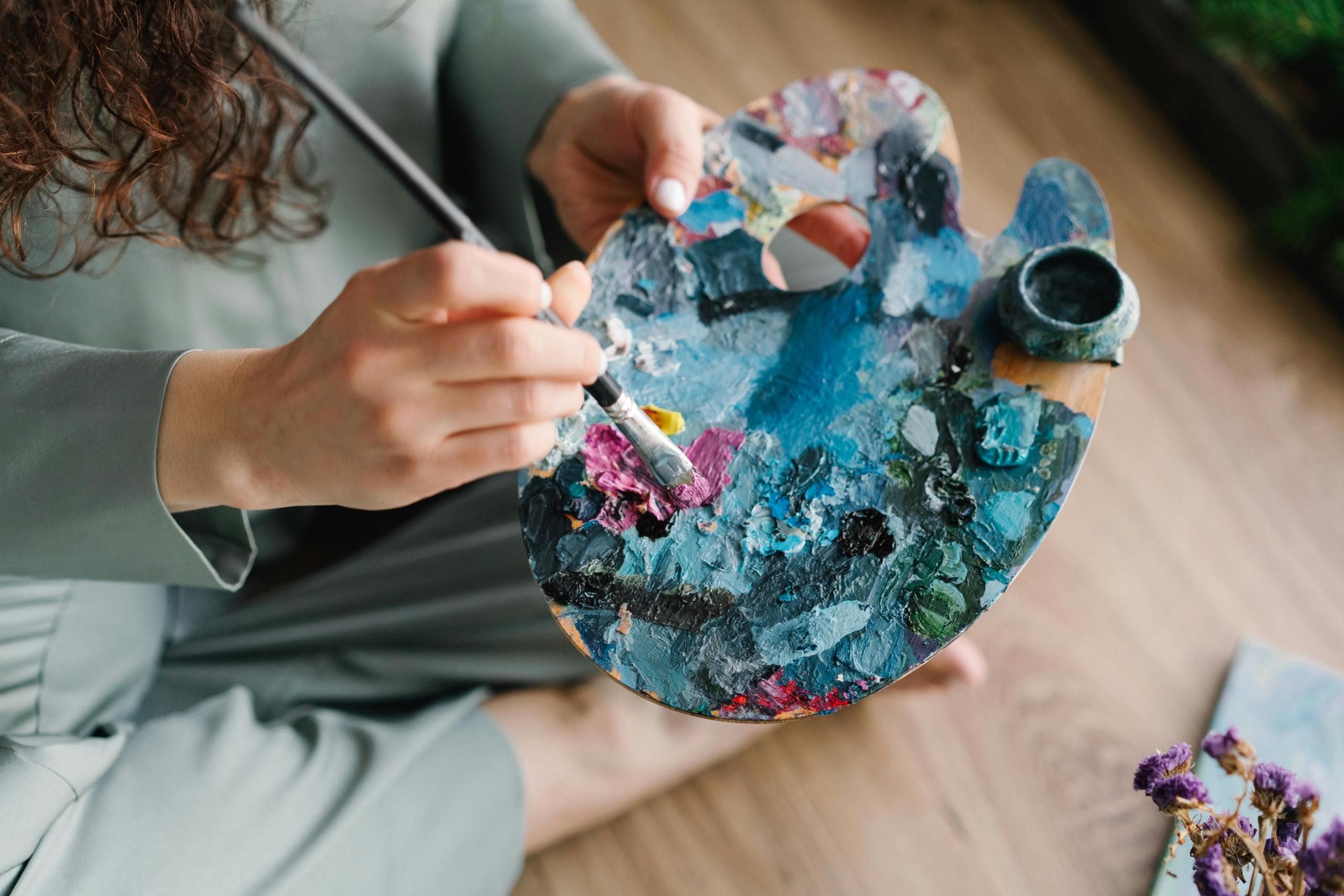 painter sitting on floor with paintbrush and artist's palette in hand