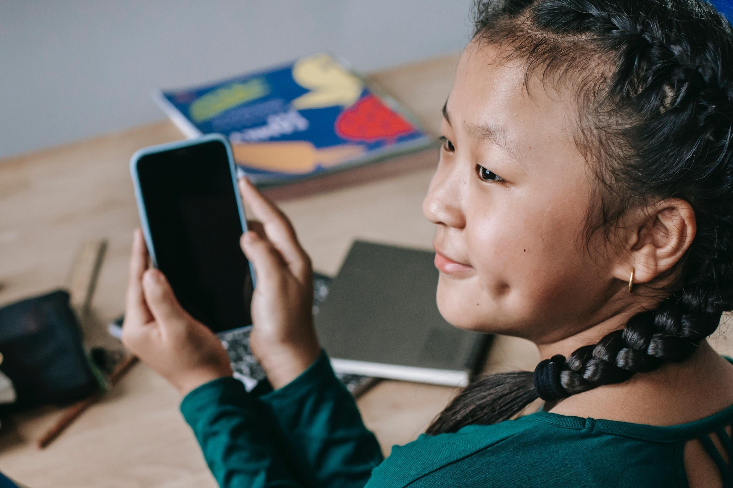 girl sitting at desk with notebooks and textbooks and holding smartphone in hands
