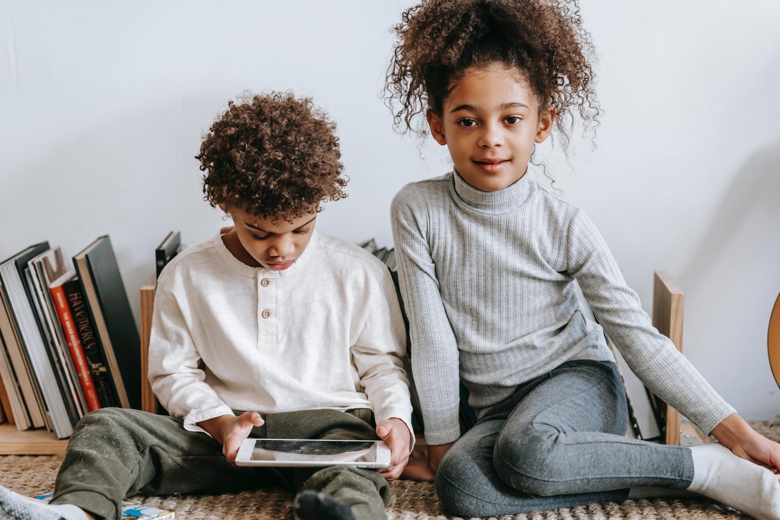 brother and sister sitting side by side on floor in front of a row of books