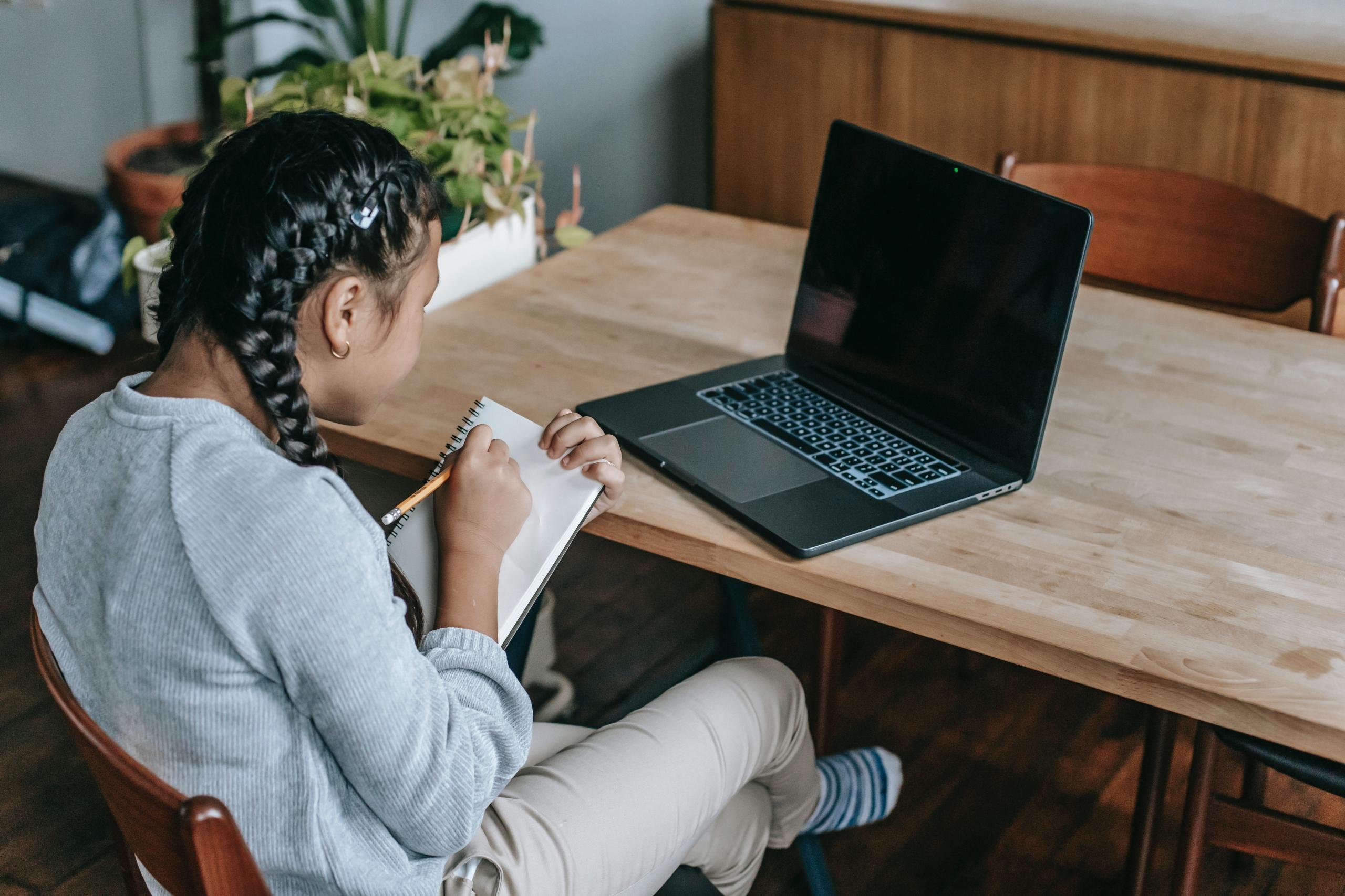 student sitting at desk with writing in notebook and looking at laptop screen