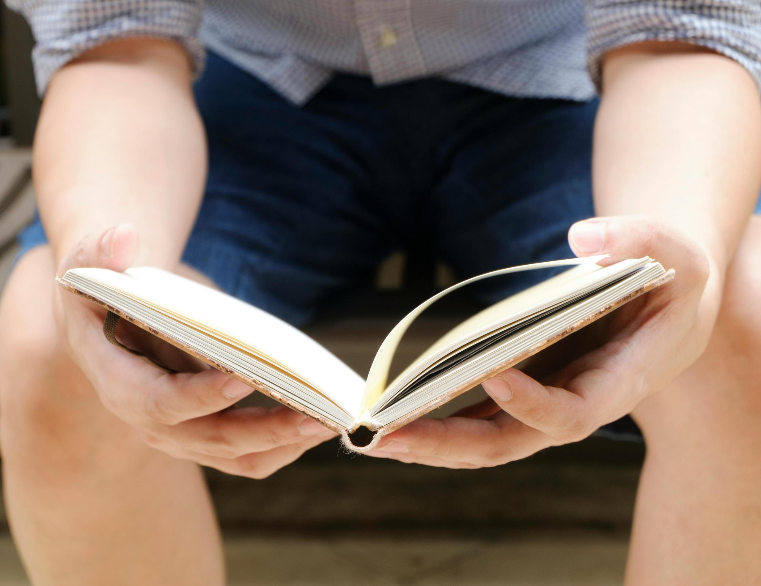 person sitting on bench outdoors leafing through a hardcover book