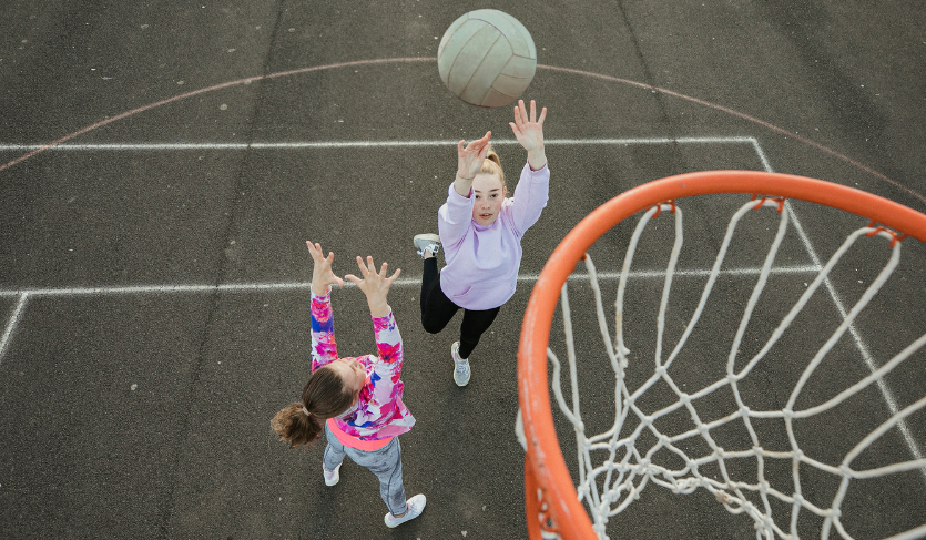 netball player shooting ball into net whilst another player tries to defend the goal