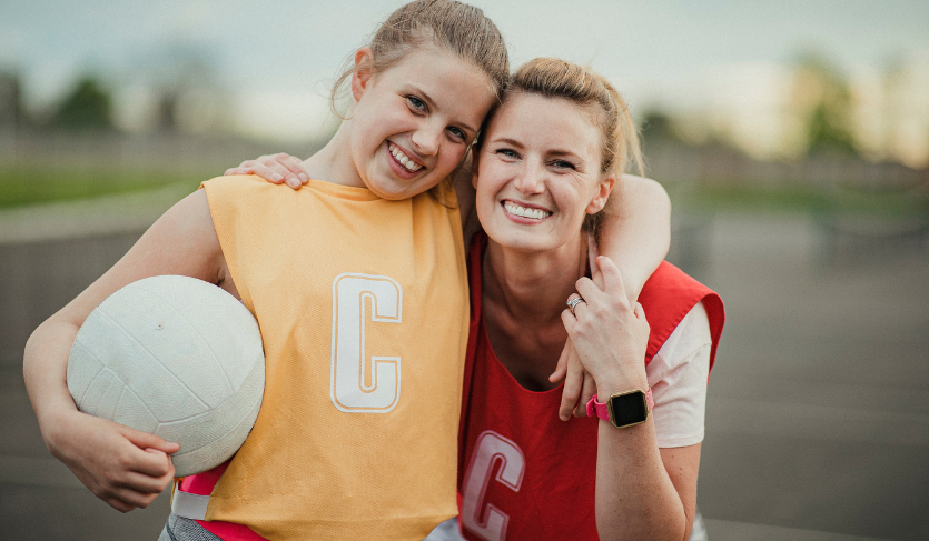 netball coach hugging netball playing who is holding a netball in her hands