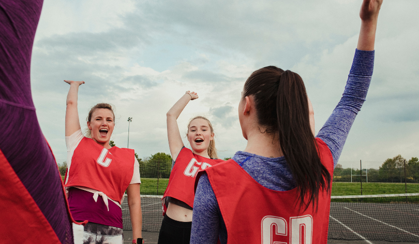 group of netball players wearing red bibs with the abbreviations of their positions