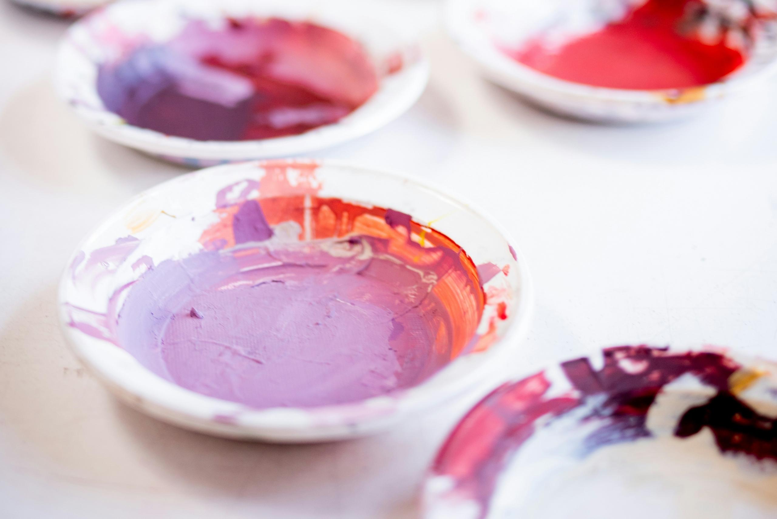 four pots on a table filled with paints in red and different shades of purple