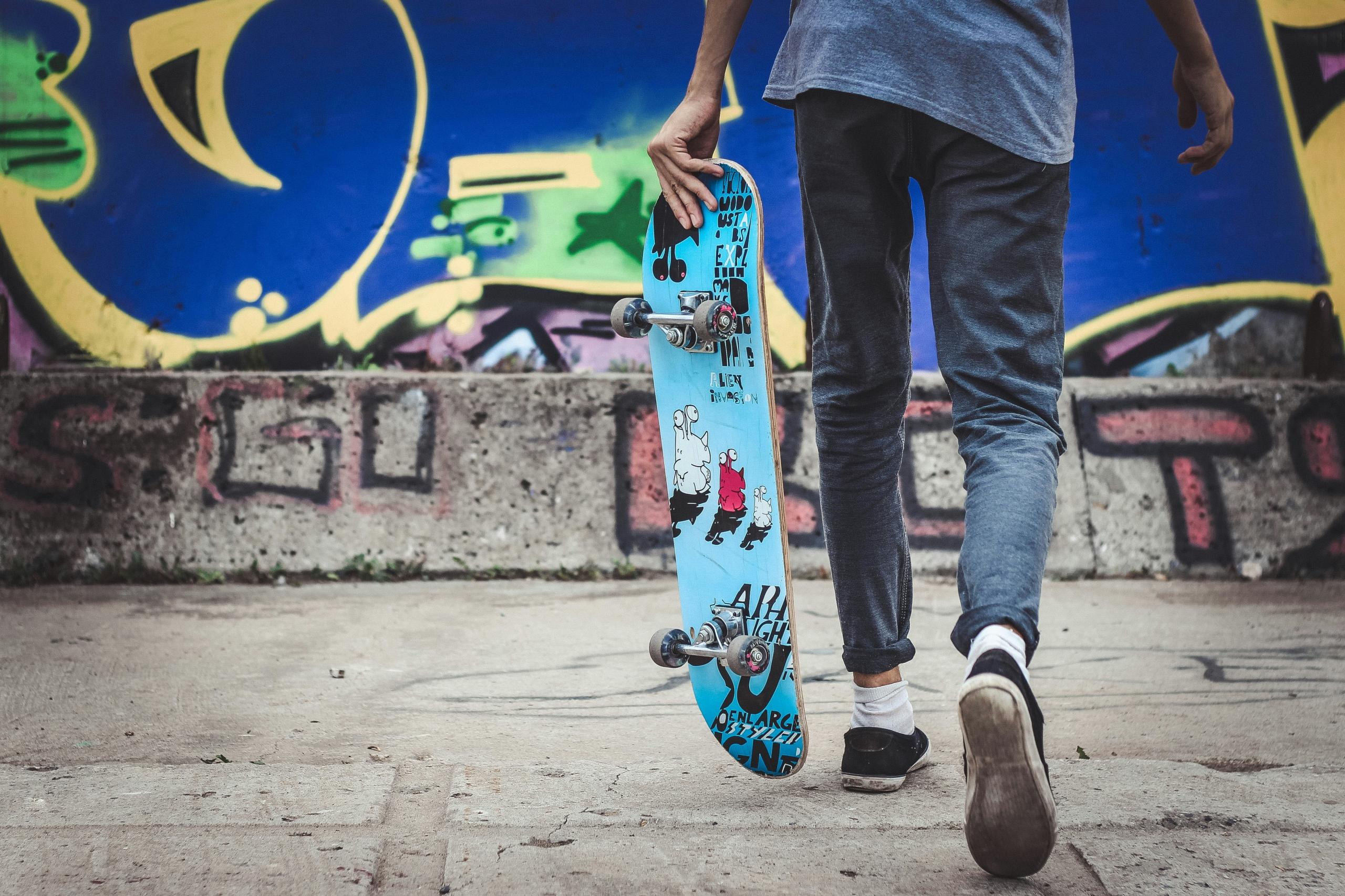 teen carrying a skateboard and walking towards a graffiti covered wall