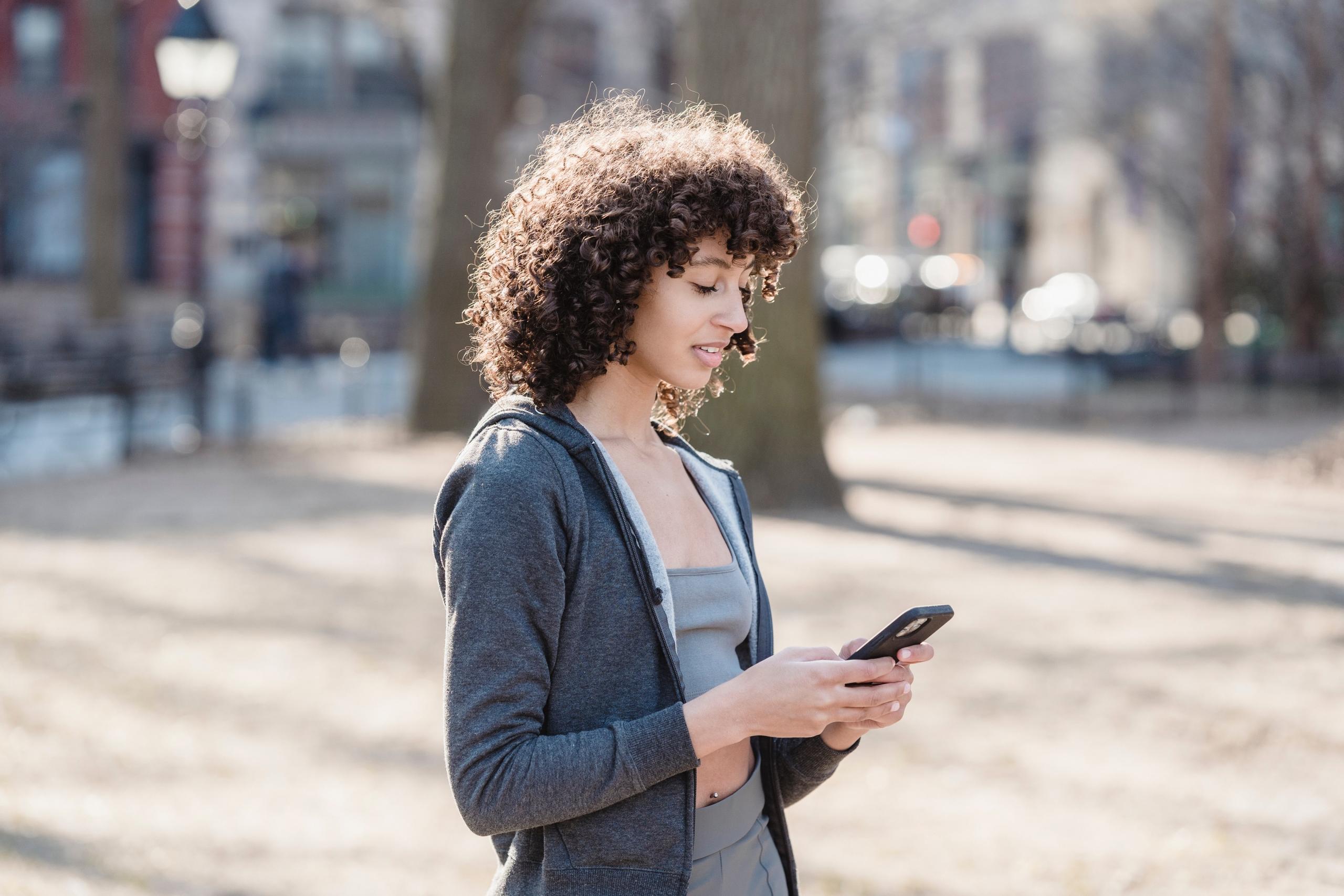 woman in fitness gear standing outside and using cellphone