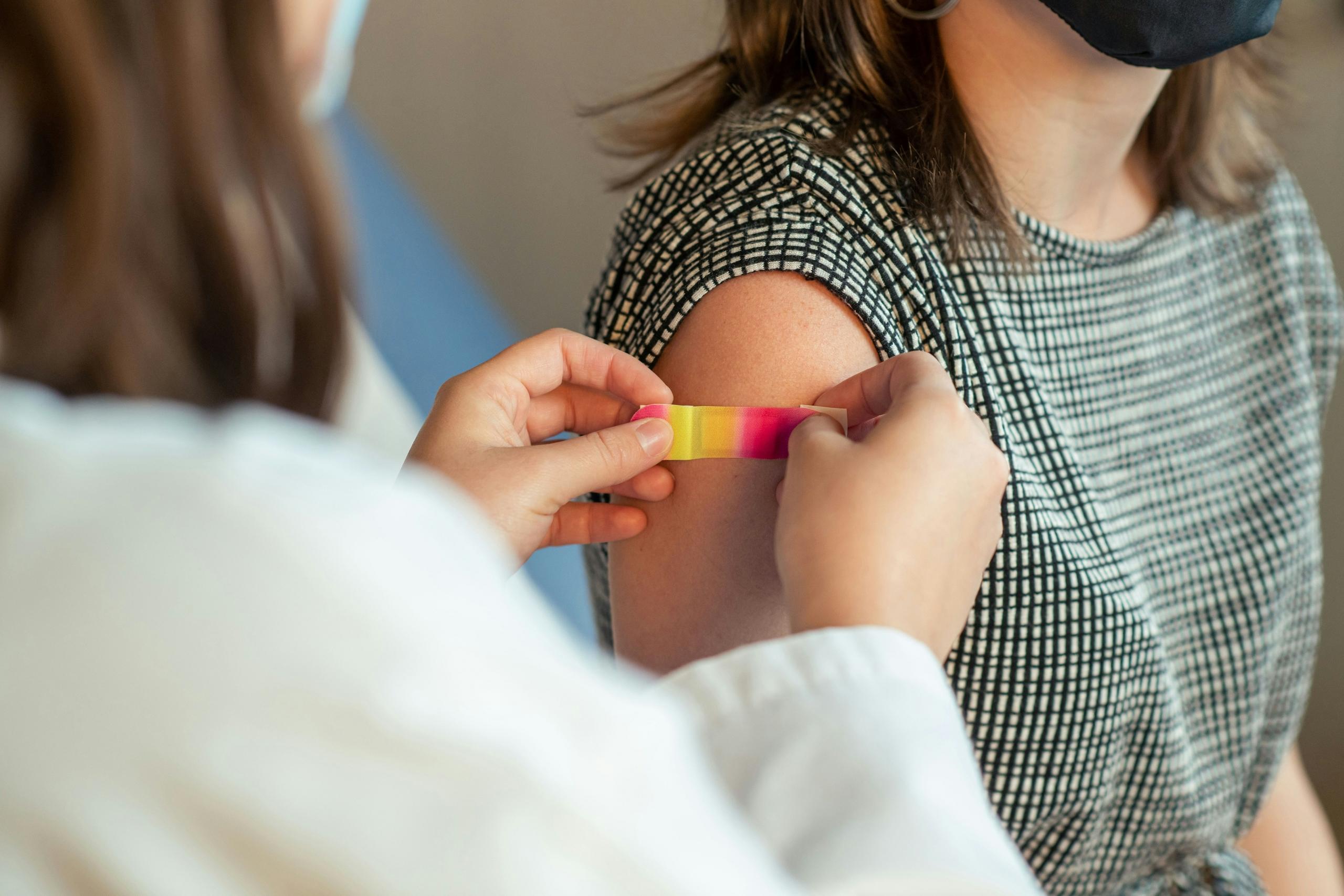 doctor in lab coat and mask applying a colourful plaster to patient's arm