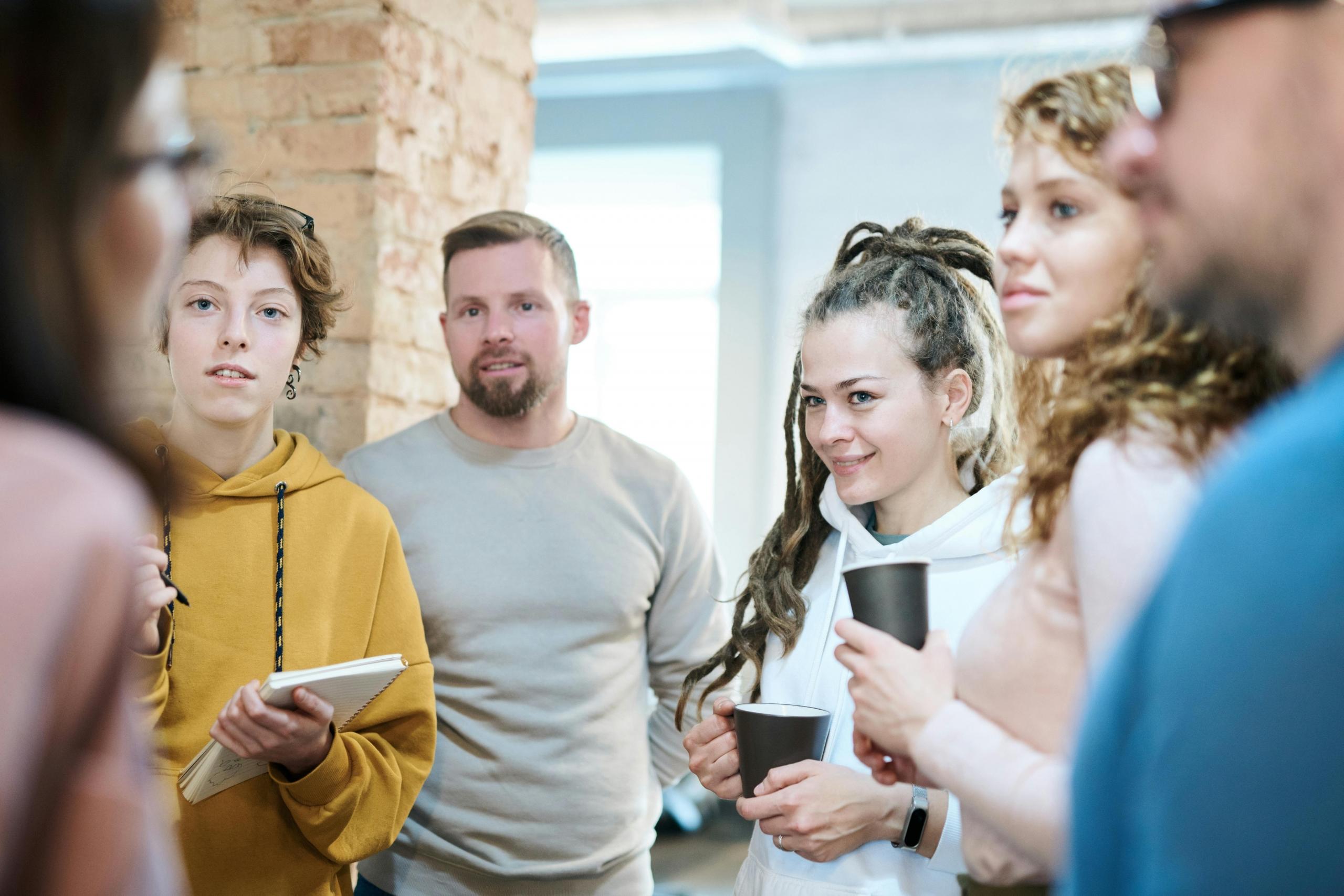 group of young people standing around in circle drinking coffee and listening to someone speak