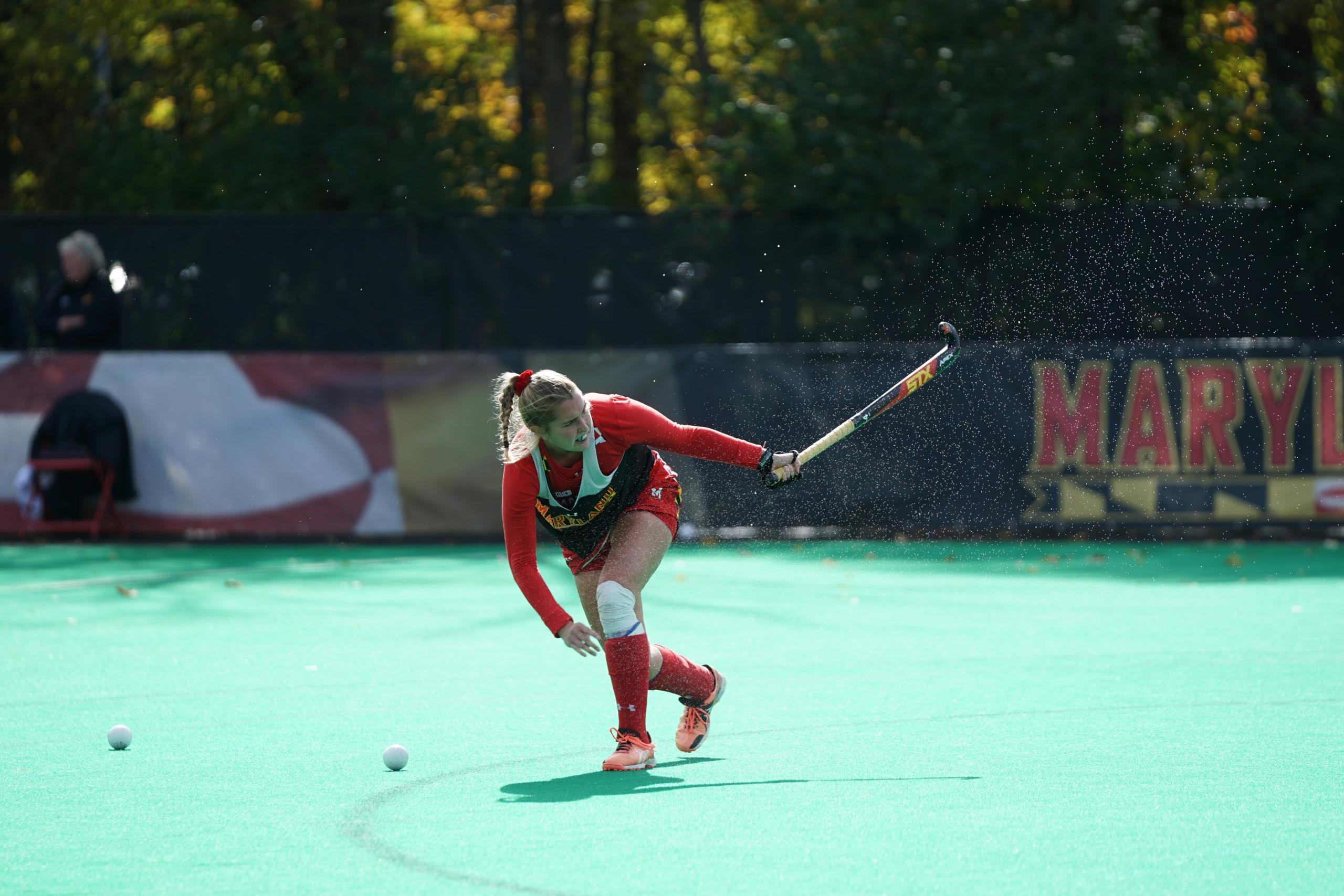 Hockey player swinging hockey stick high into the air behind her