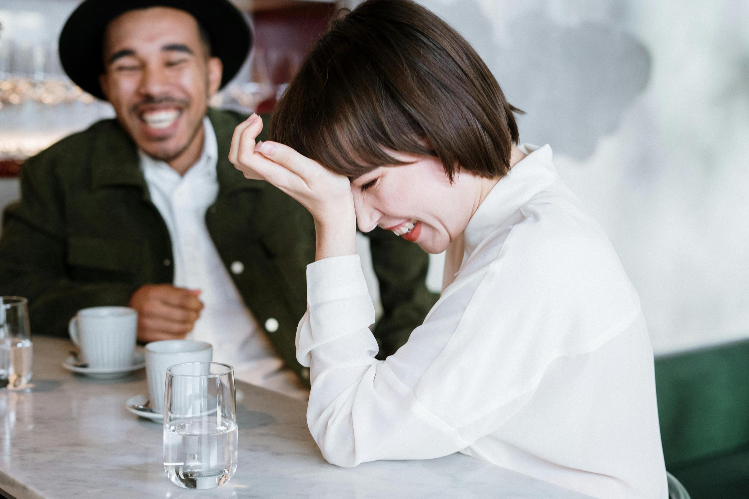 woman in white dress shirt drinking coffee with man wearing wide-brimmed hat