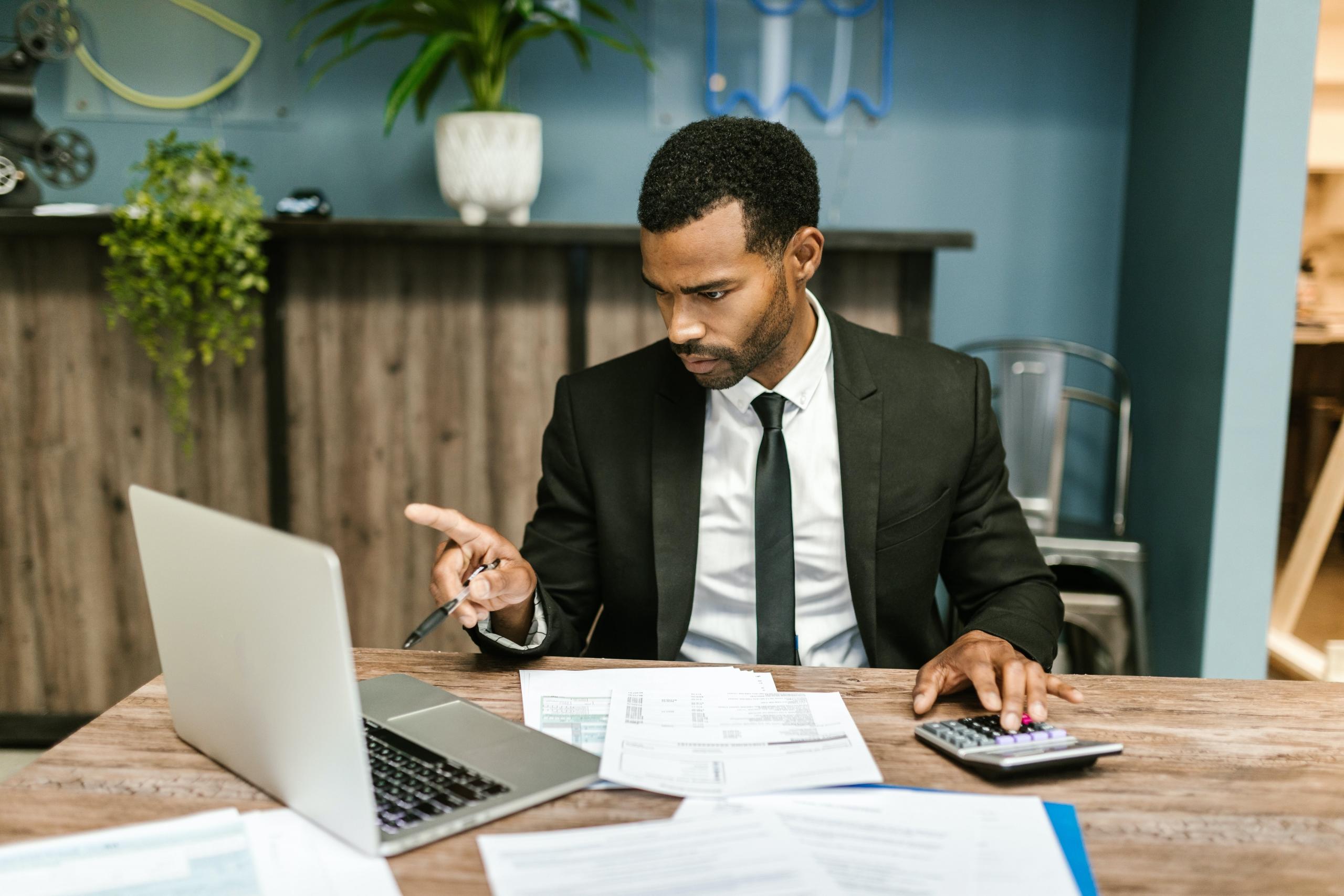 accountant sated behind desk using laptop and calculator while looking at financial documents