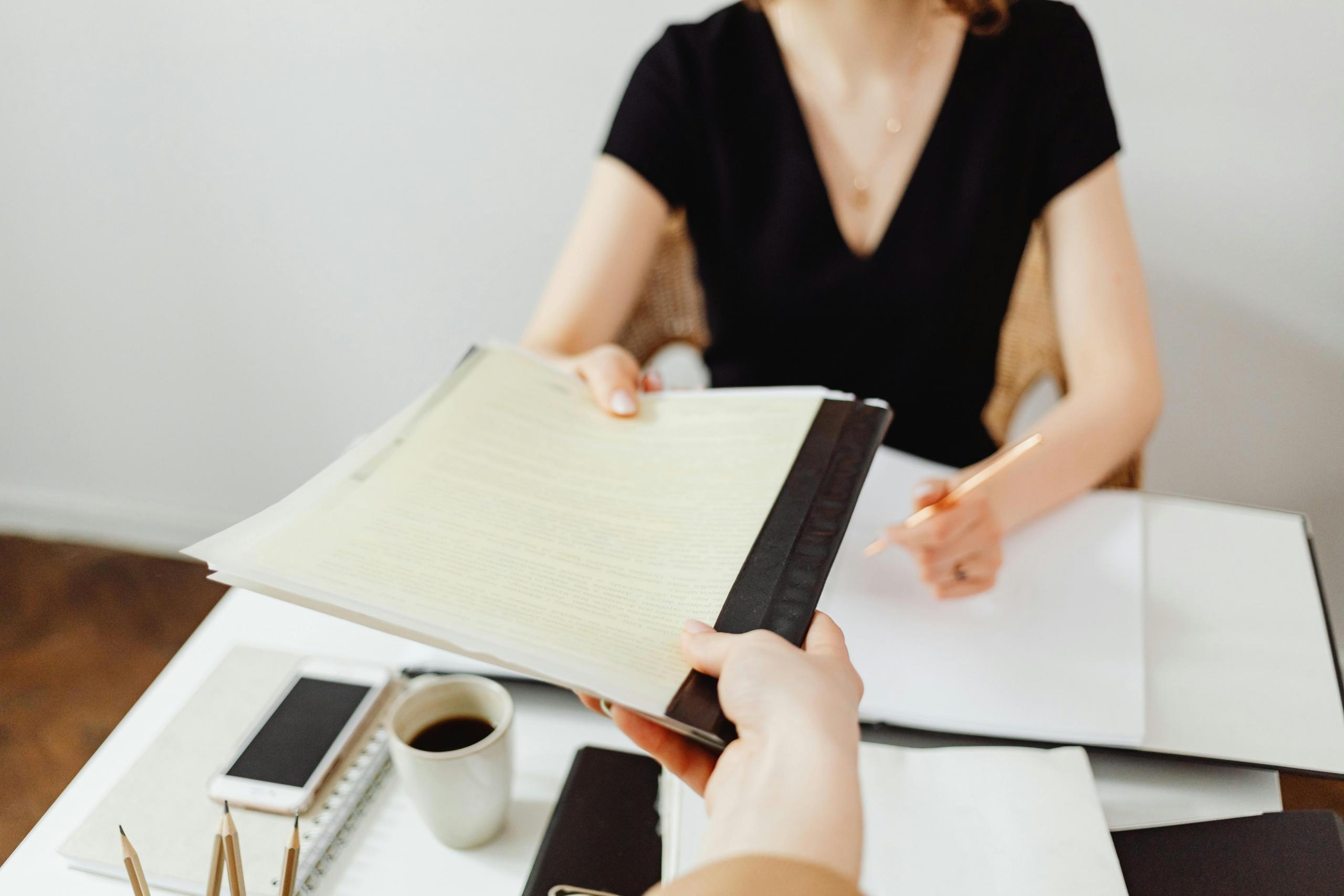 woman seated behind a desk handing over a document to her colleague