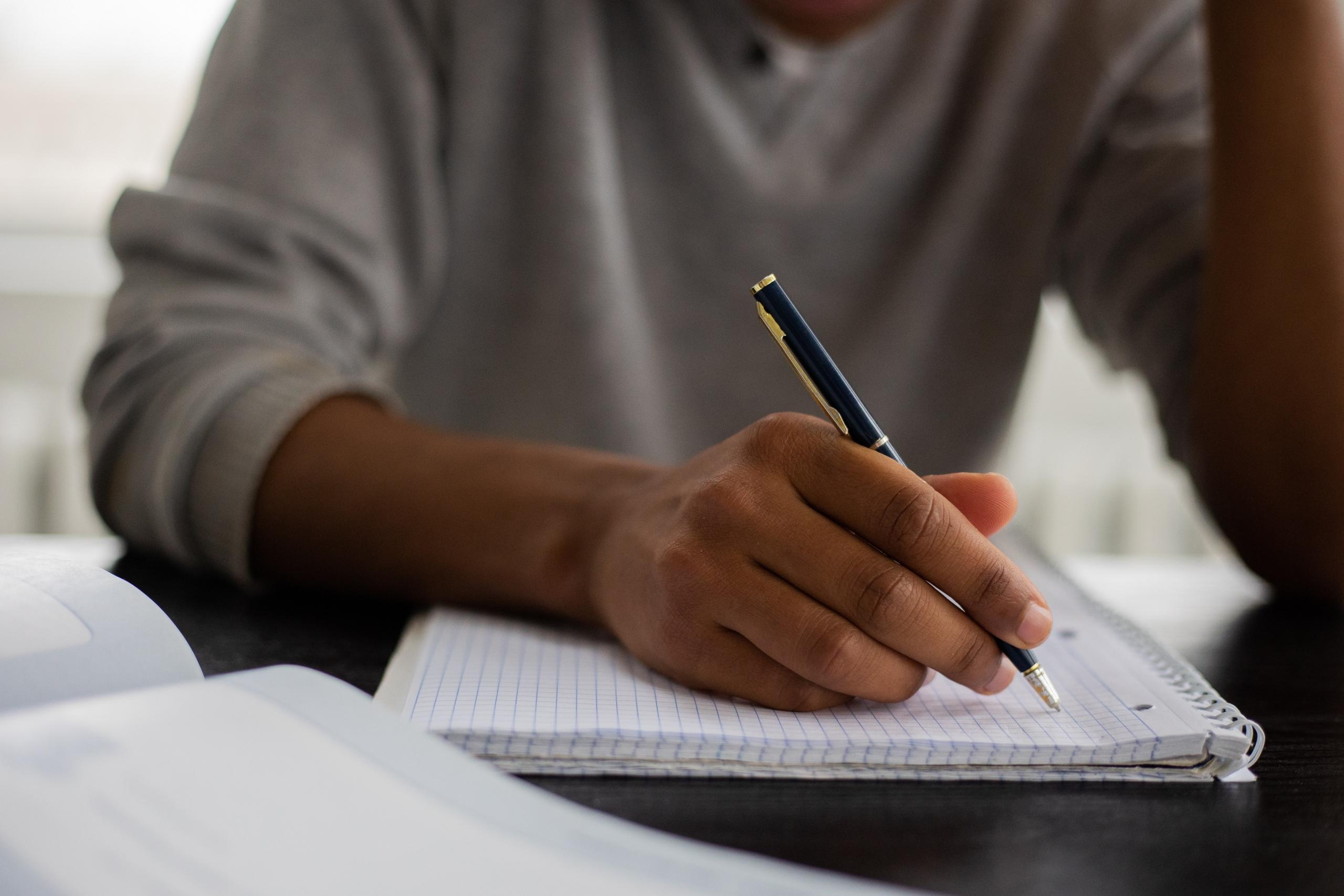student in grey top writing on notepad