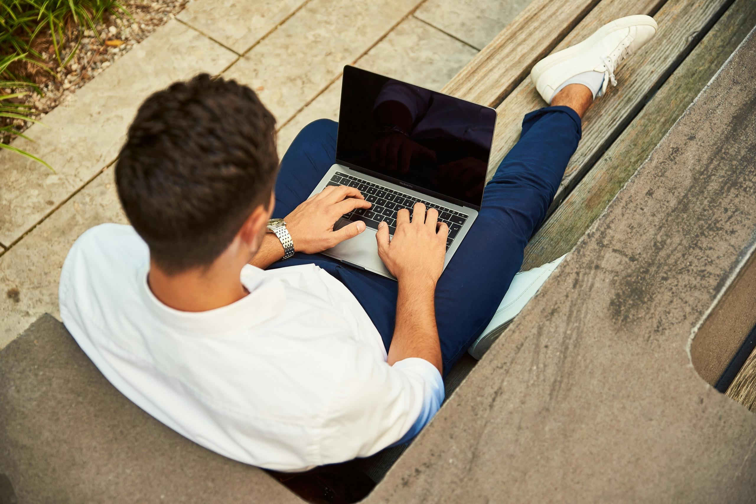 man sitting on the floor outside typing on laptop