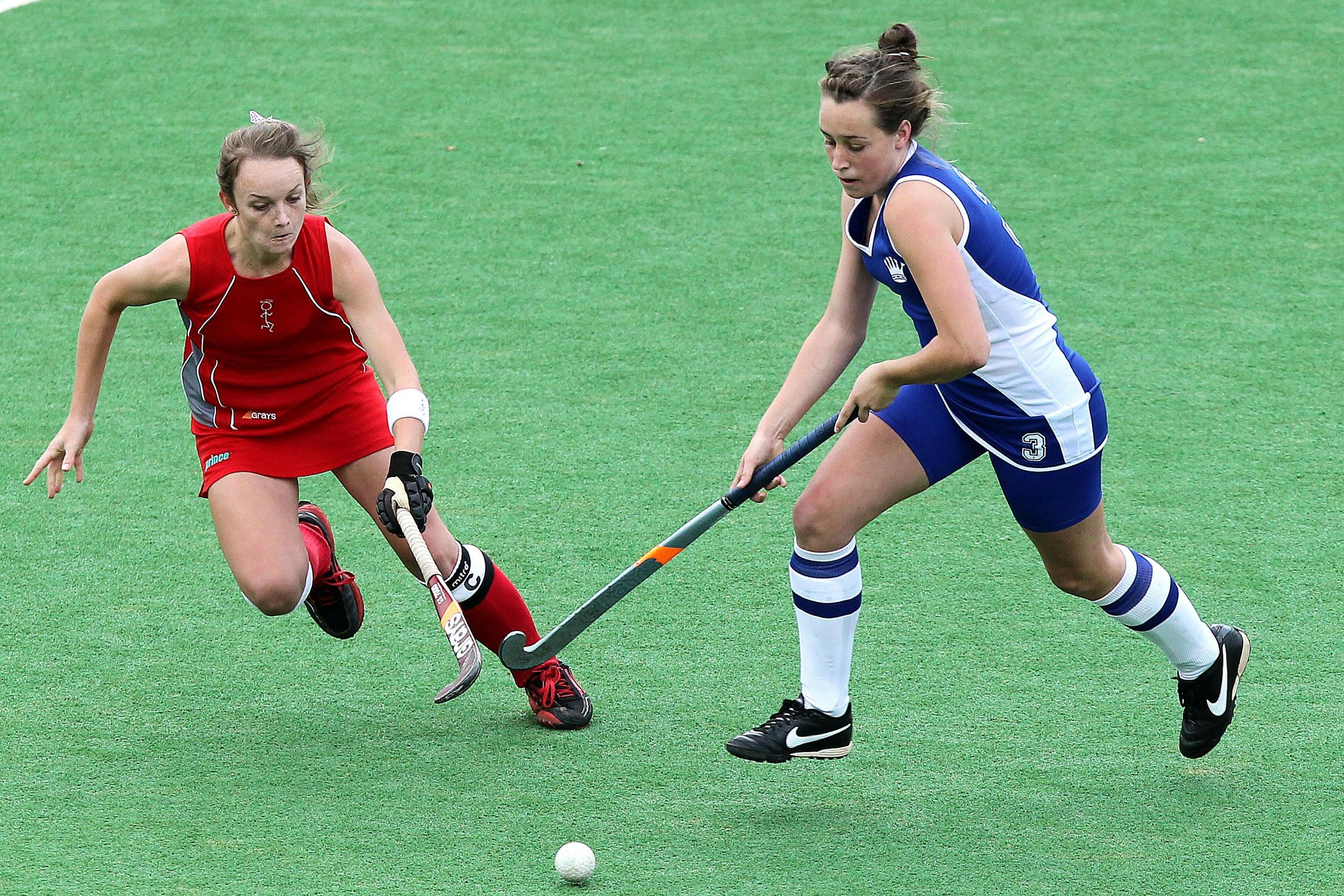 two hockey players on the field chasing after the ball with their hockey sticks stretched out in front of them