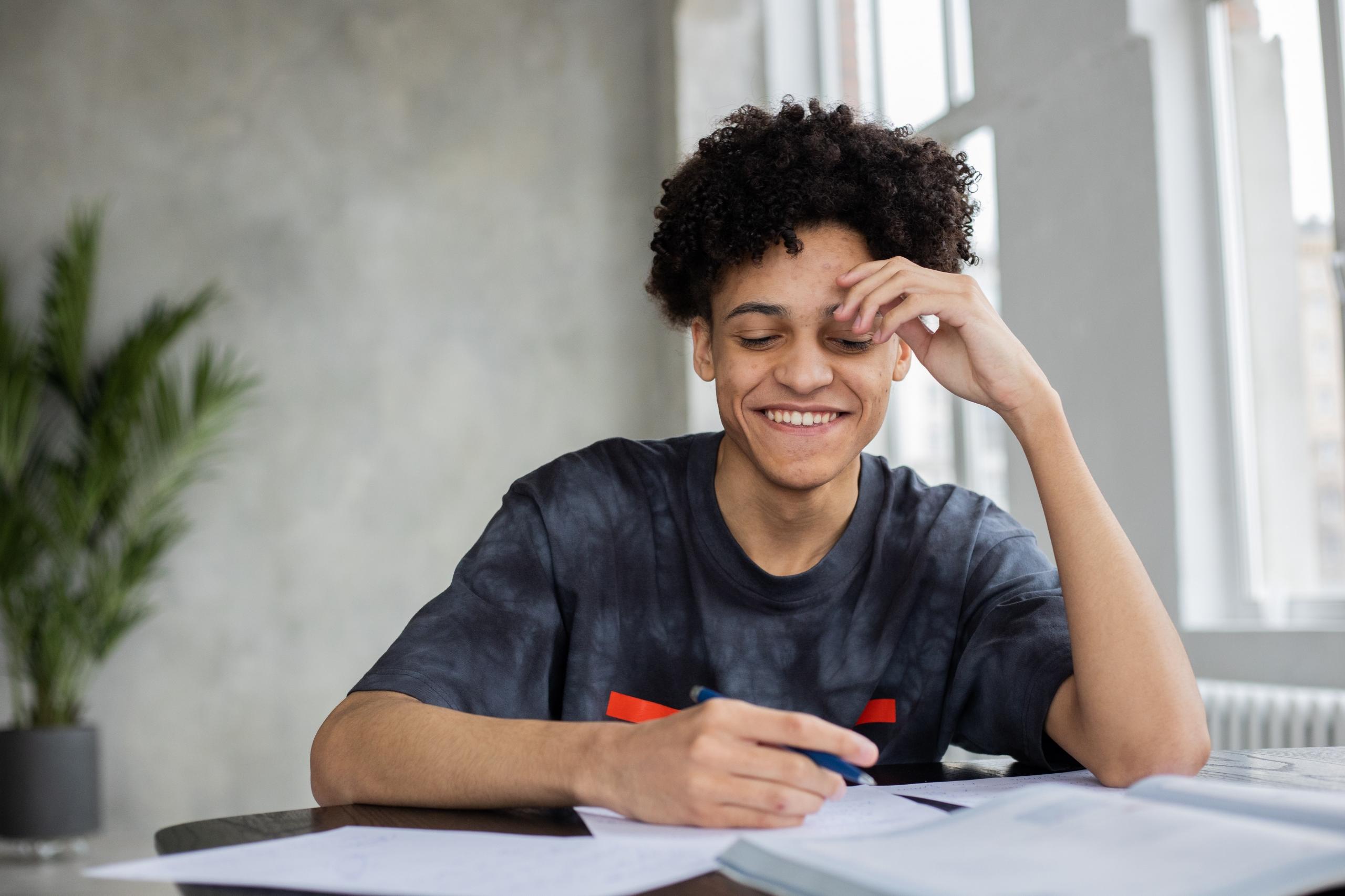 high school student sitting at desk reading textbook and writing in notebook