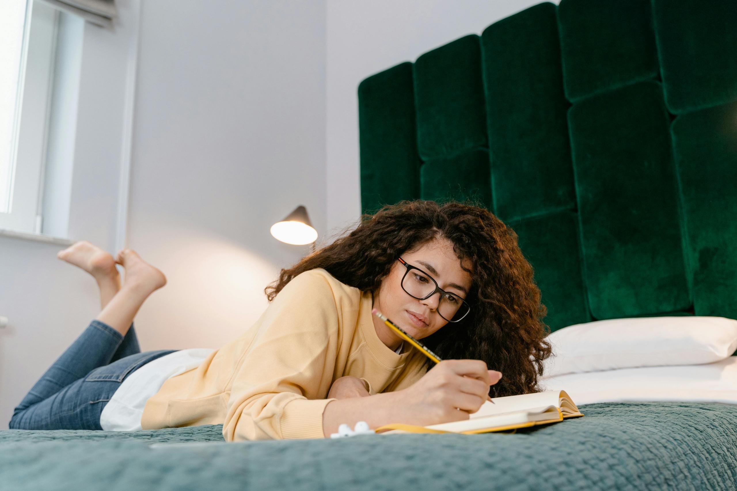 girl lying on top of bed writing in a notebook