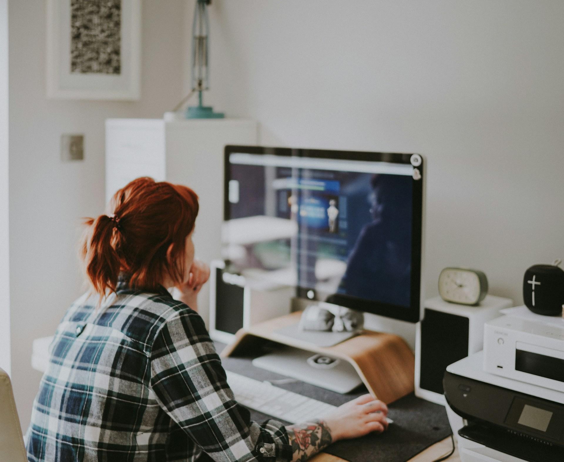 woman in check shirt leaning forward to look at computer monitor