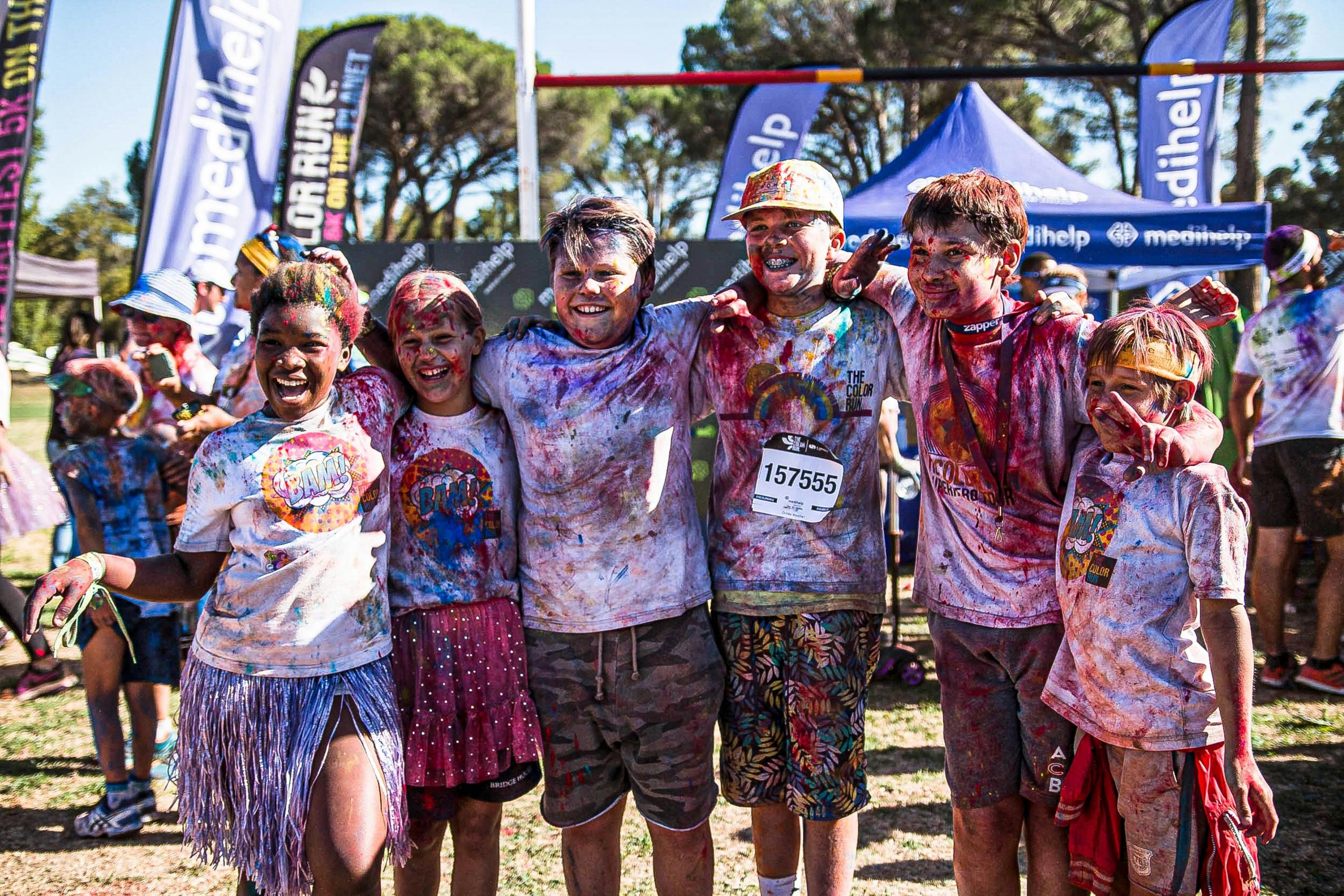 group of laughing children with arms around each other covered in paint at the end of a race