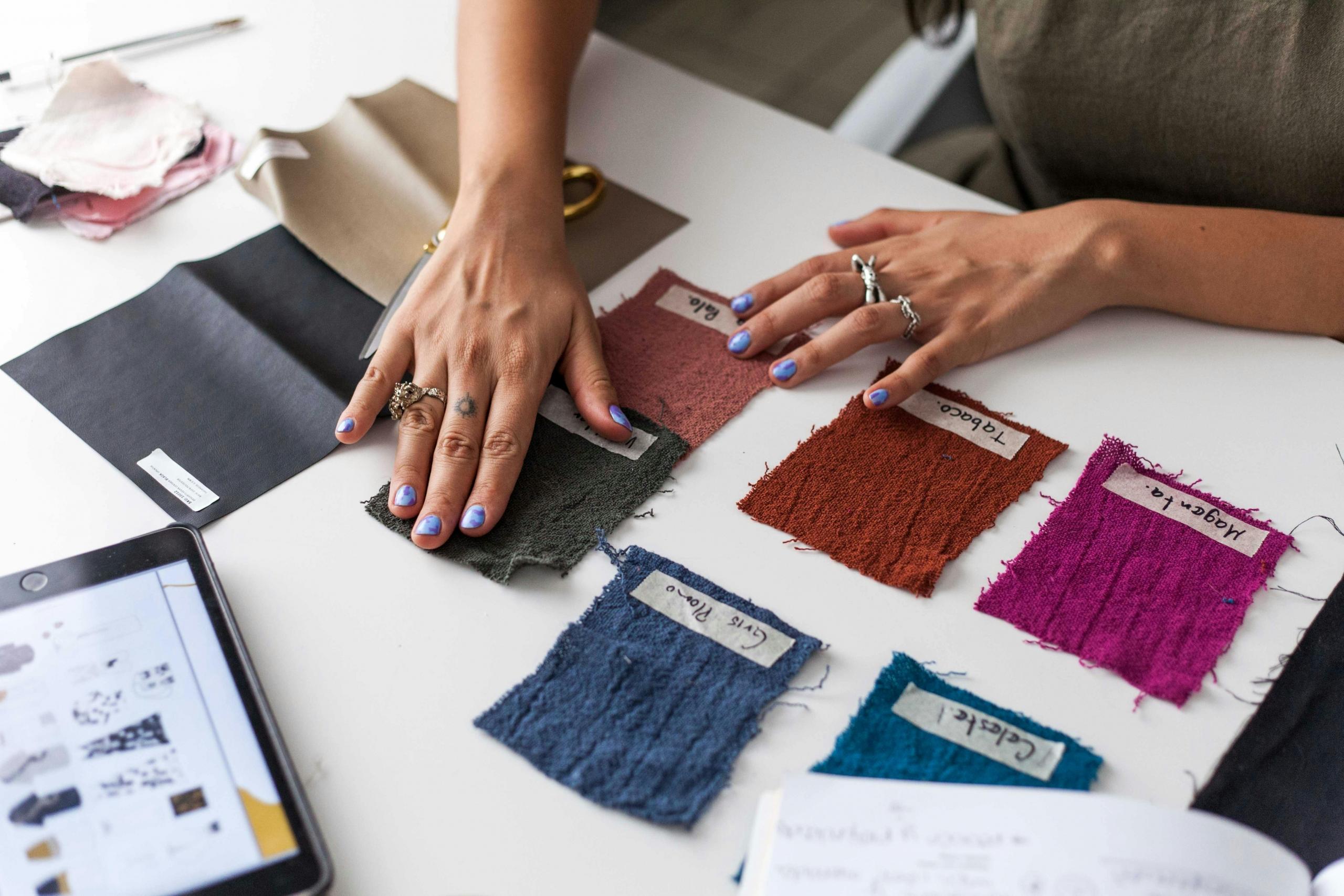 designers placing different fabric samples on desk next to fashion illustration on electronic tablet