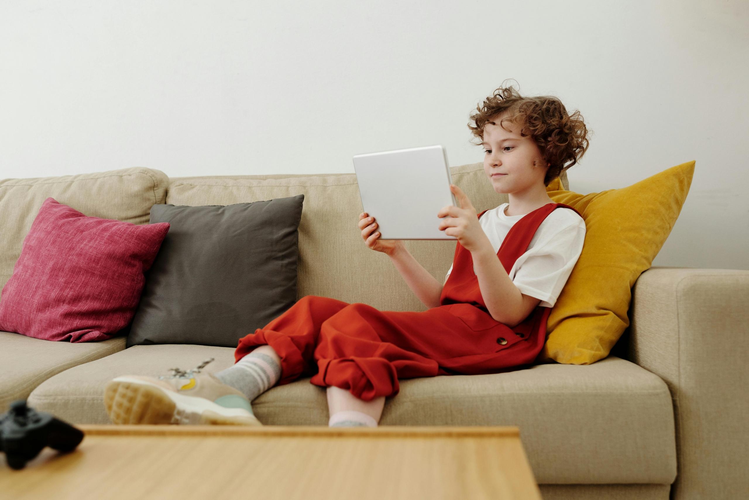 child sitting on couch reading on electronic tablet
