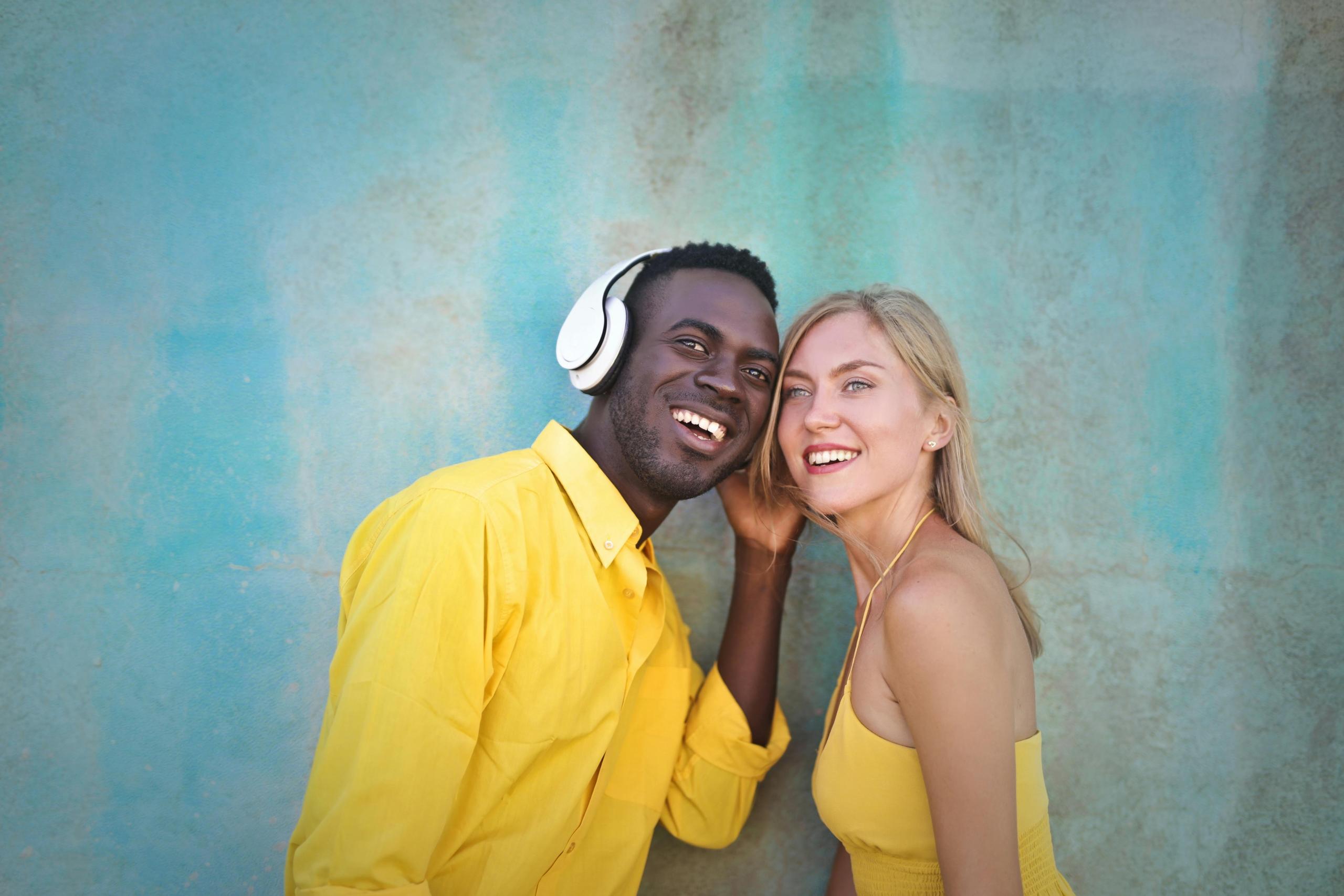 man and woman wearing canary yellow tops and sharing a set of white headphones