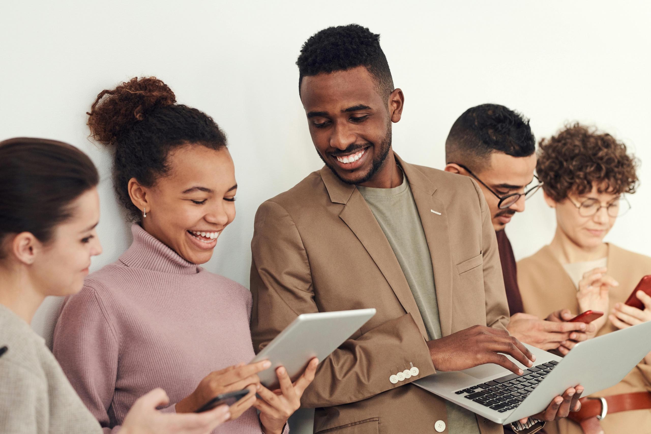colleagues standing side by side looking at laptops, smartphones, and tablets