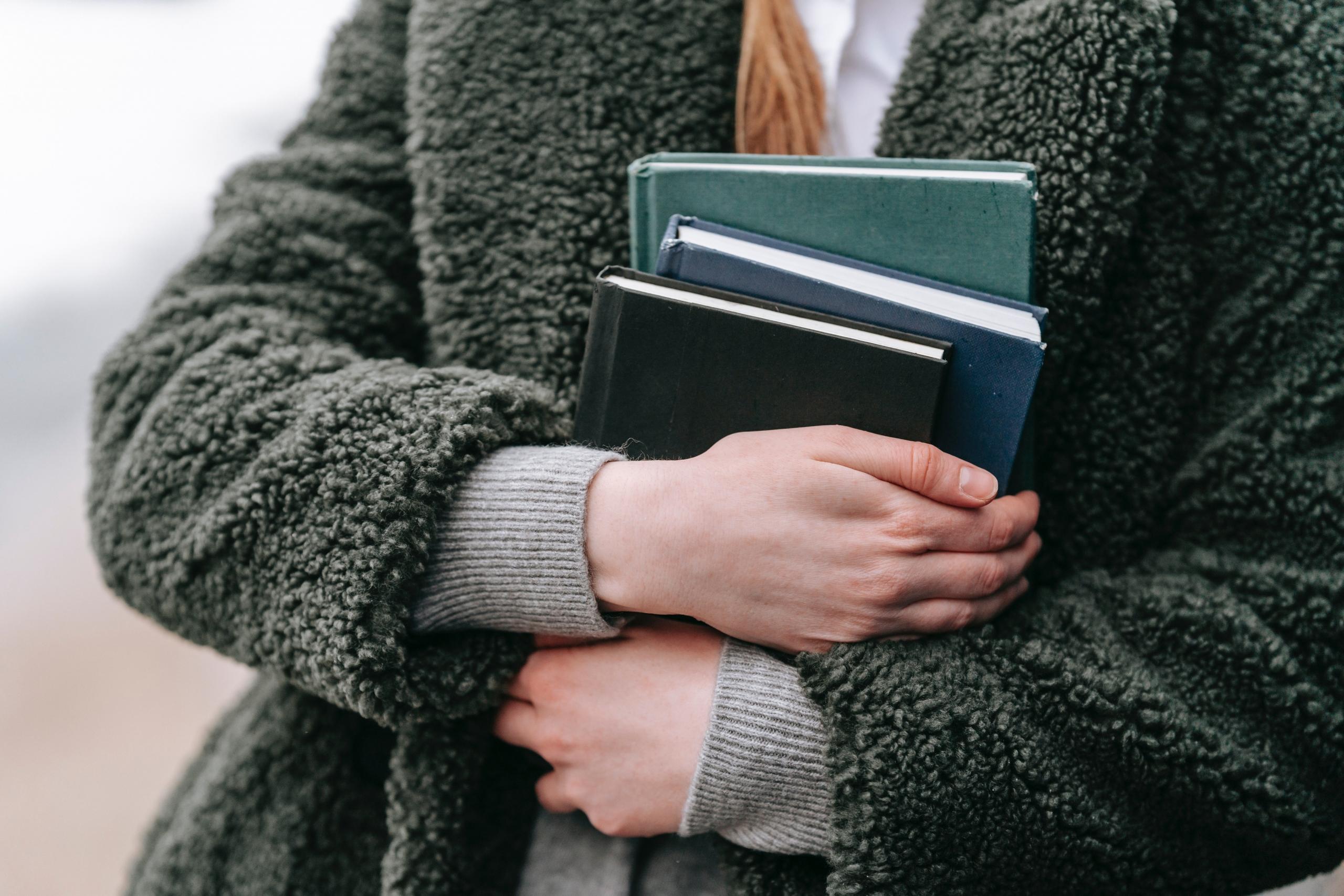 student wearing green teddy coat clutching three books to her chest