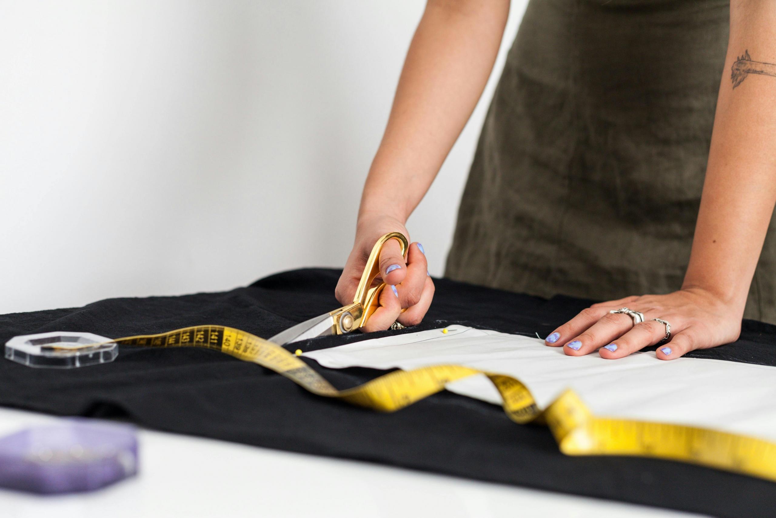 seamstress using dressmaking scissors and yellow tape measure to cut fabric using a pattern