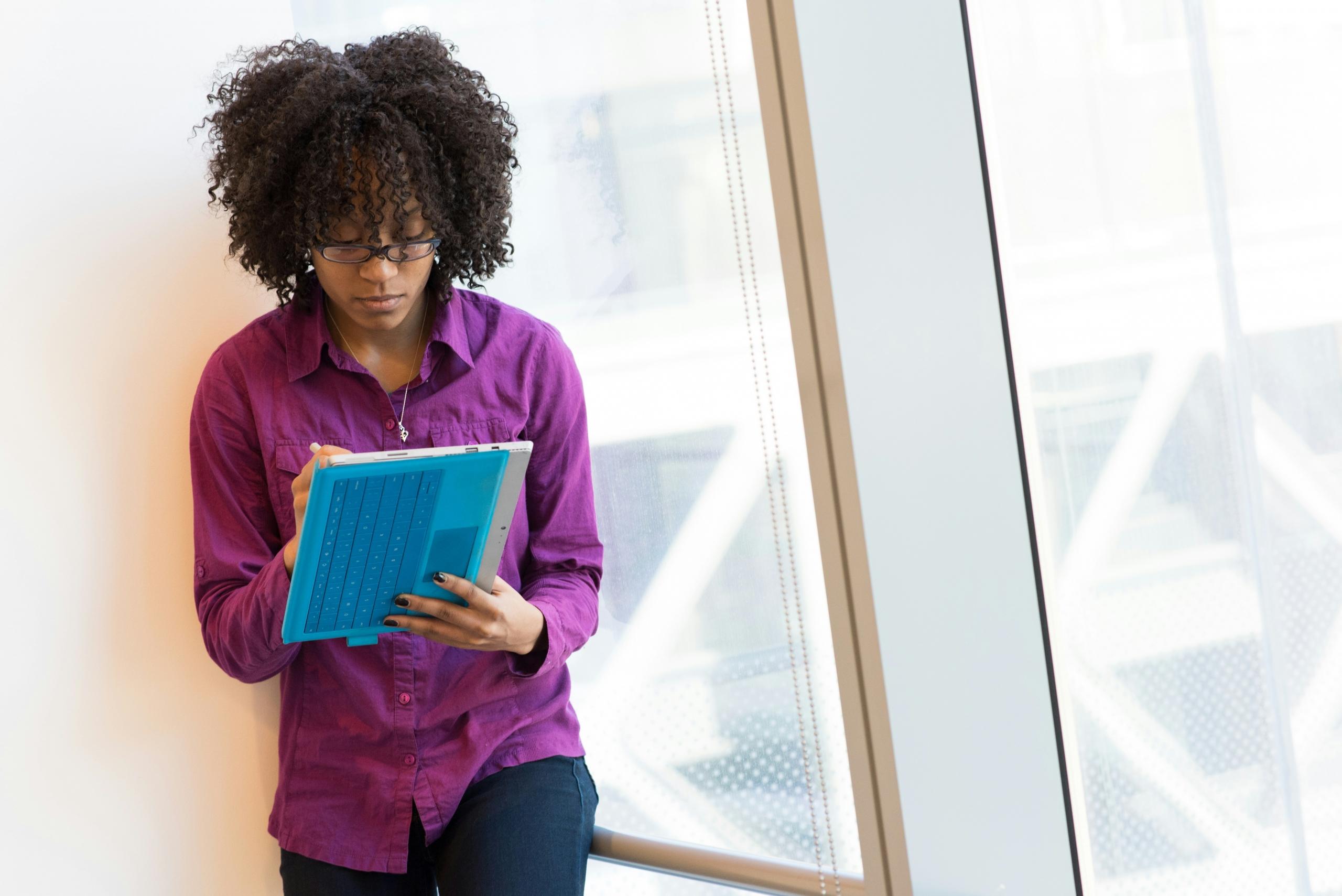 woman wearing violet shirt standing in window working on iPad