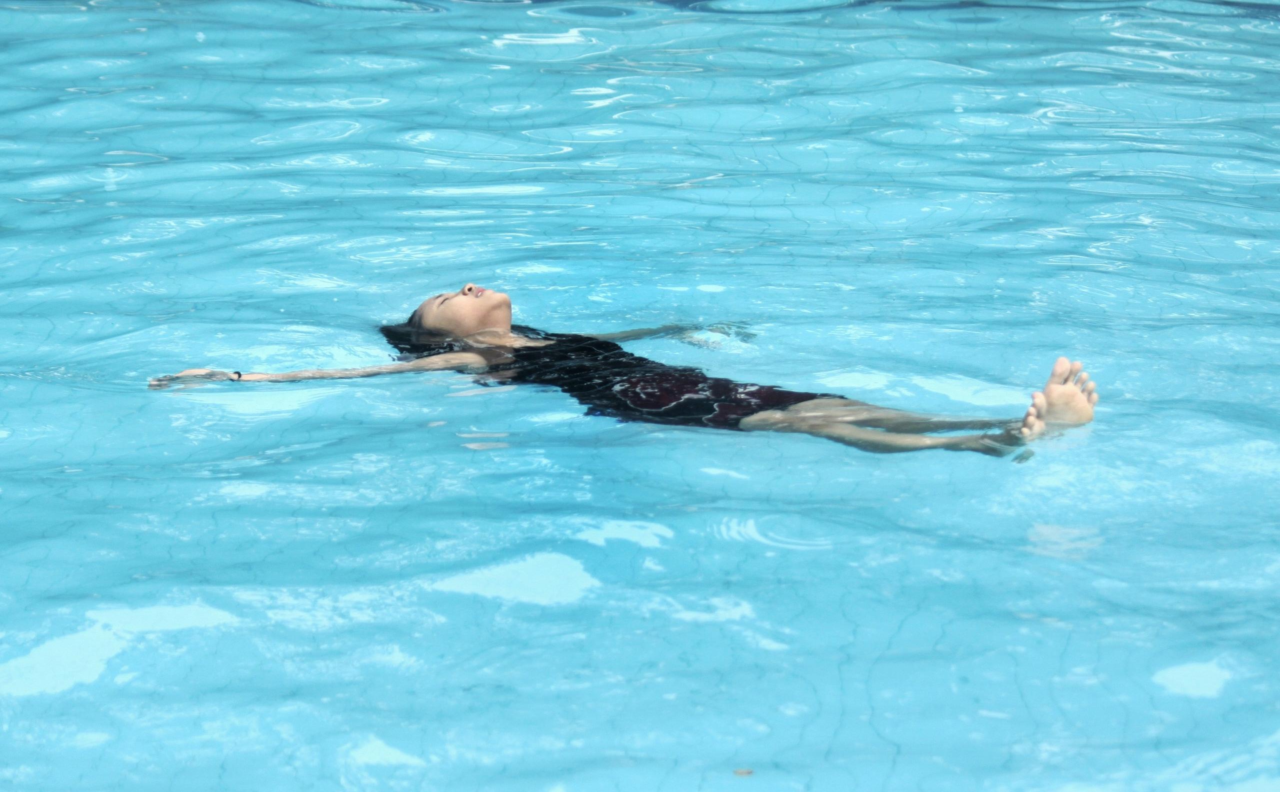 girl in pool floating on her back with arms outstretched