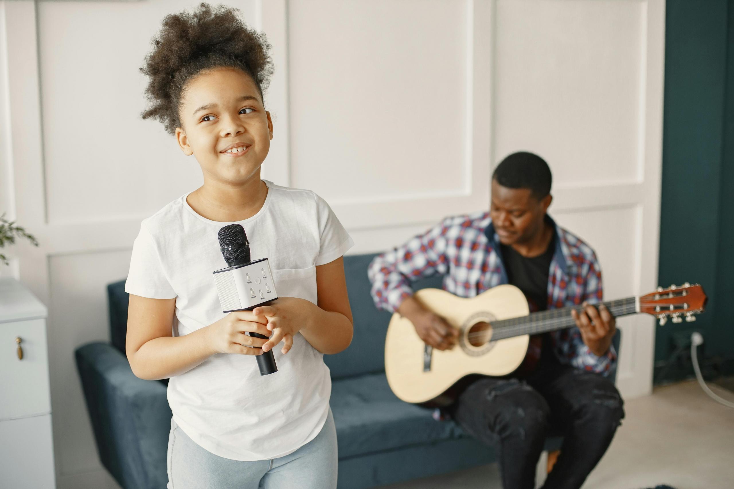 girl standing in living room holding microphone while singing teacher plays guitar in background
