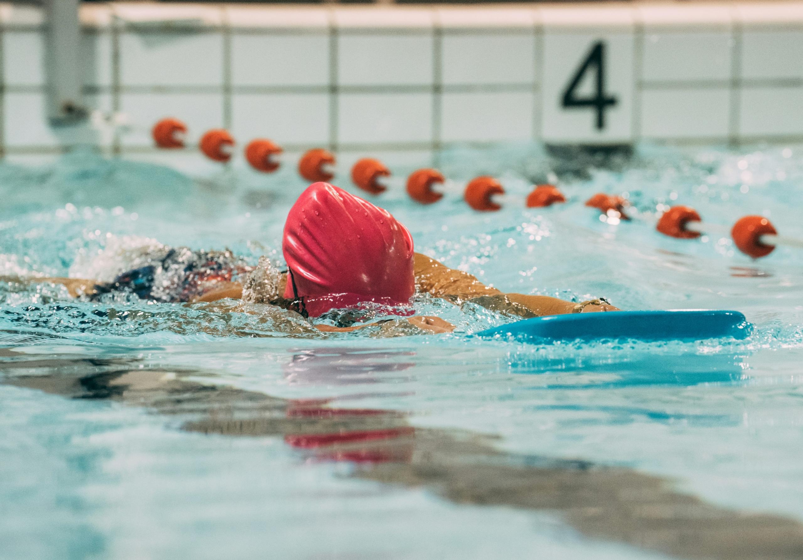 child learning to swim in lanes in pool wearing red swimming cap