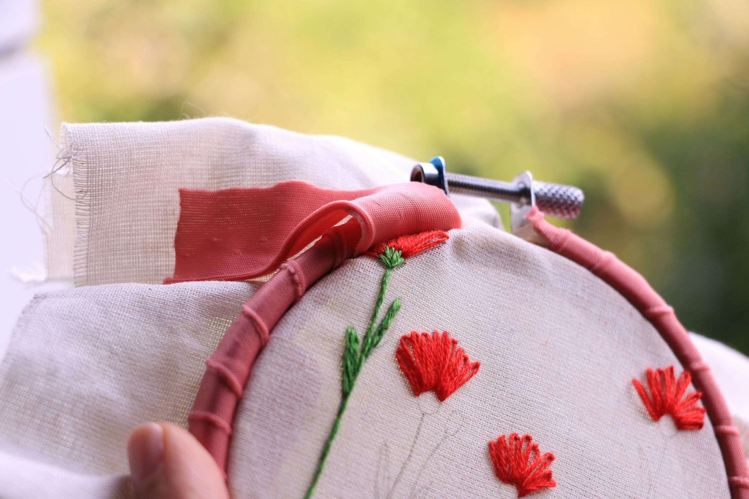 person embroidering red flowers on cream fabric