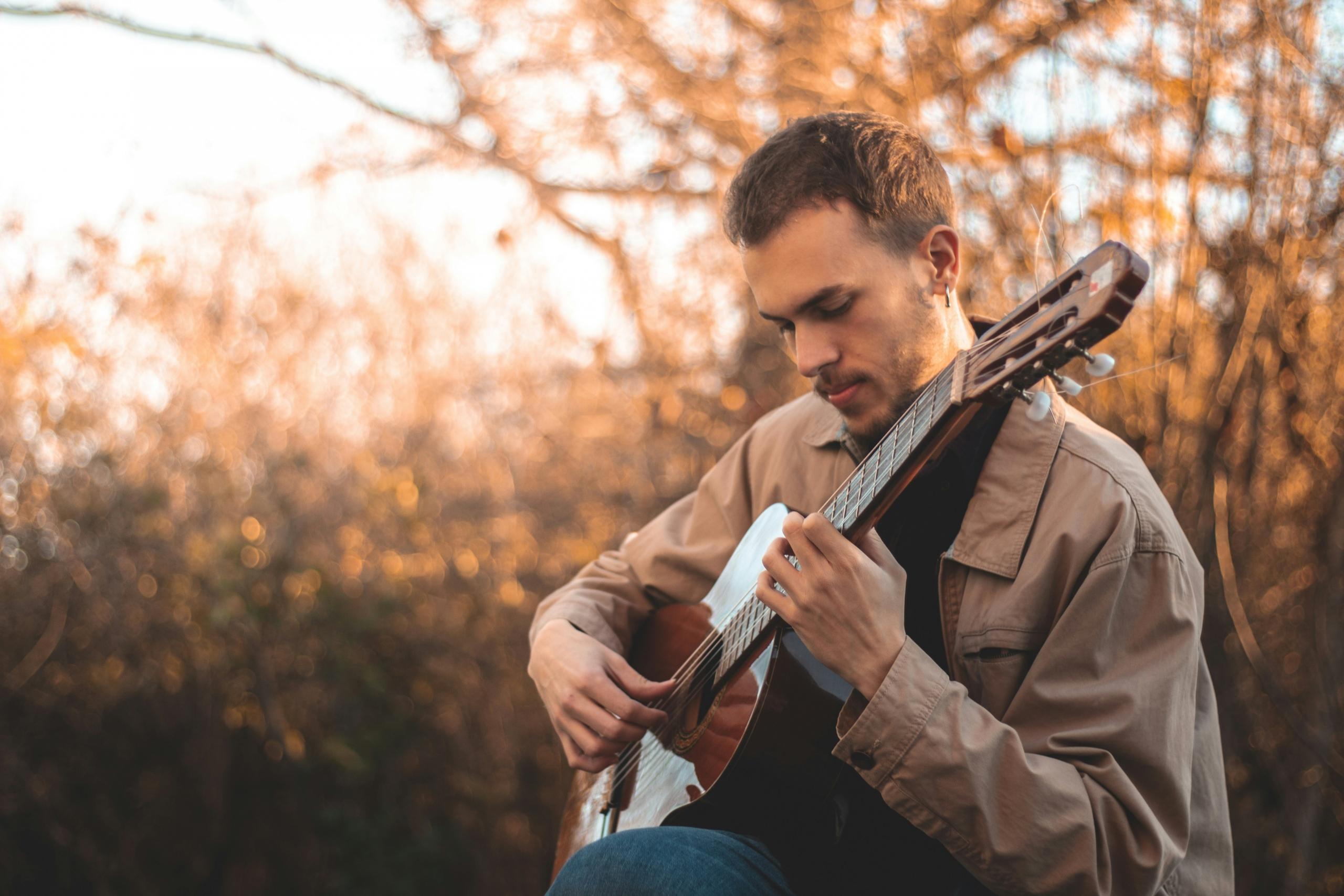 man paying guitar outside near trees at sunset