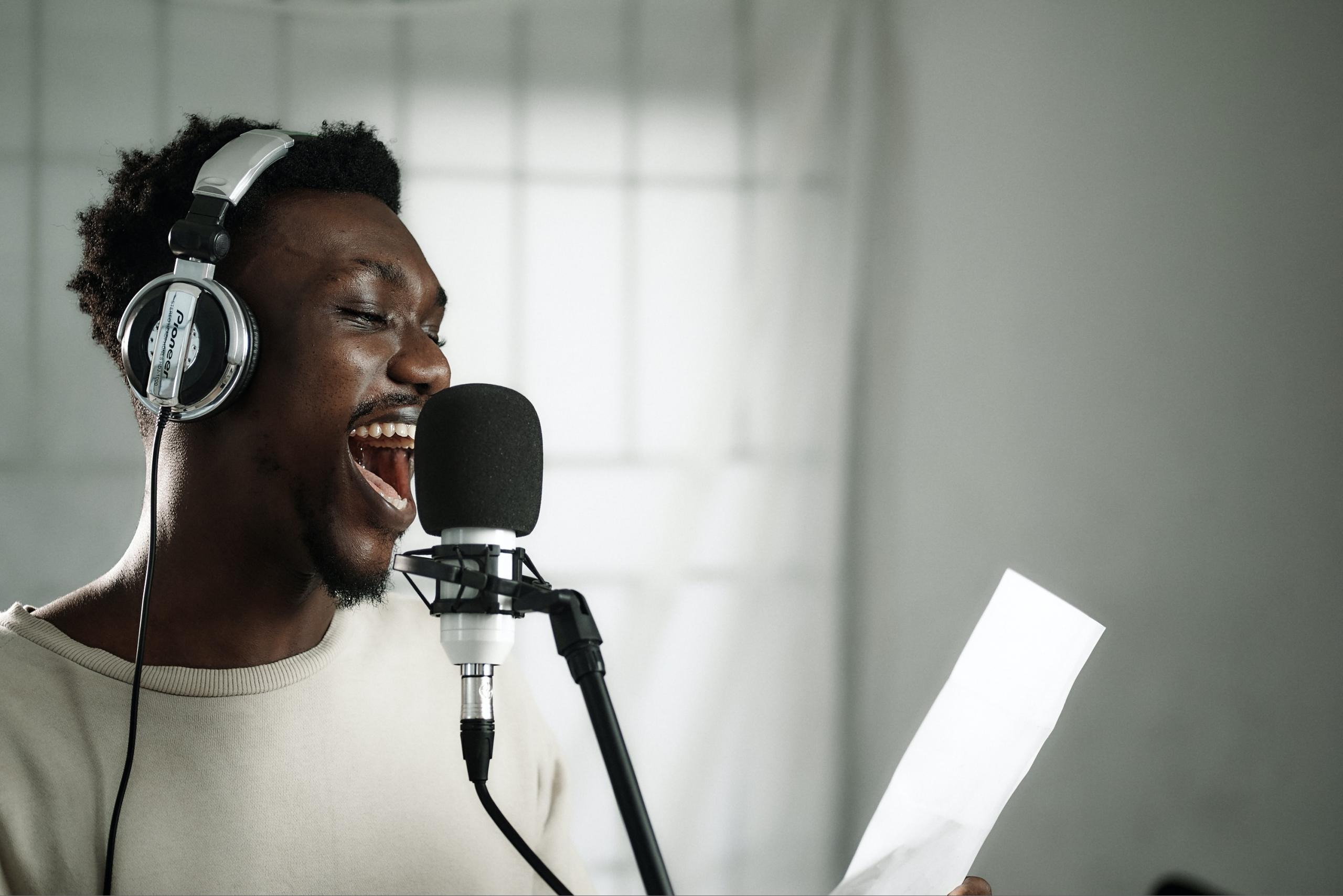singer in studio wearing headphones and reading lyrics on sheet of paper