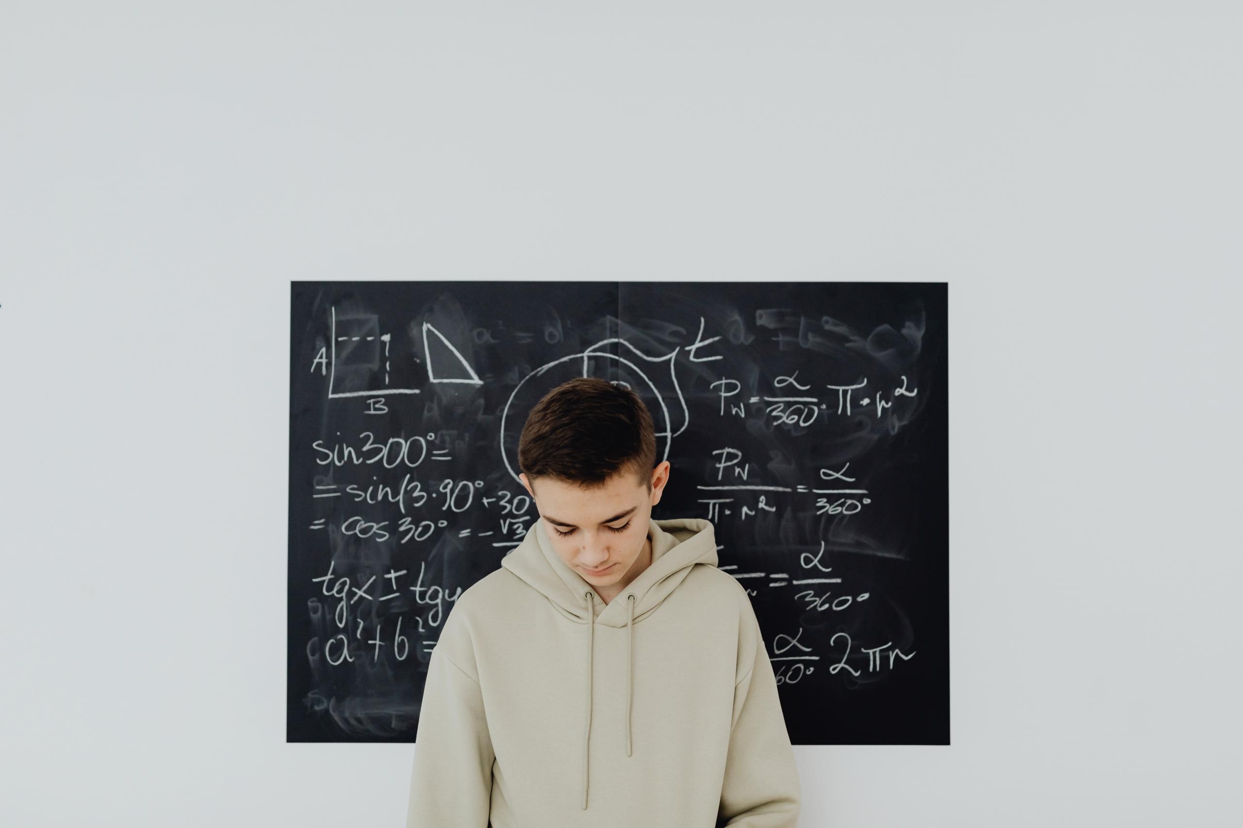 student standing in front of blackboard with maths problems written on it