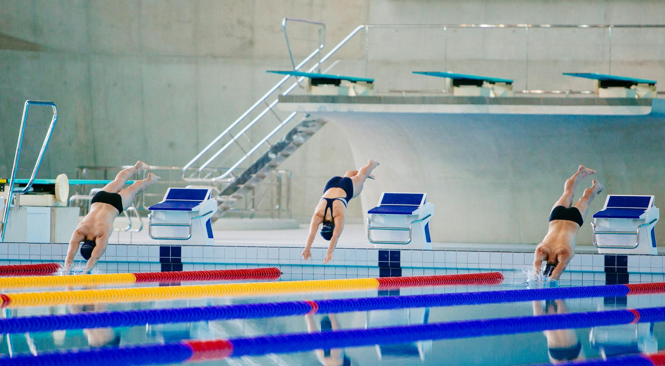 three swimmers diving into pool in synchronisation