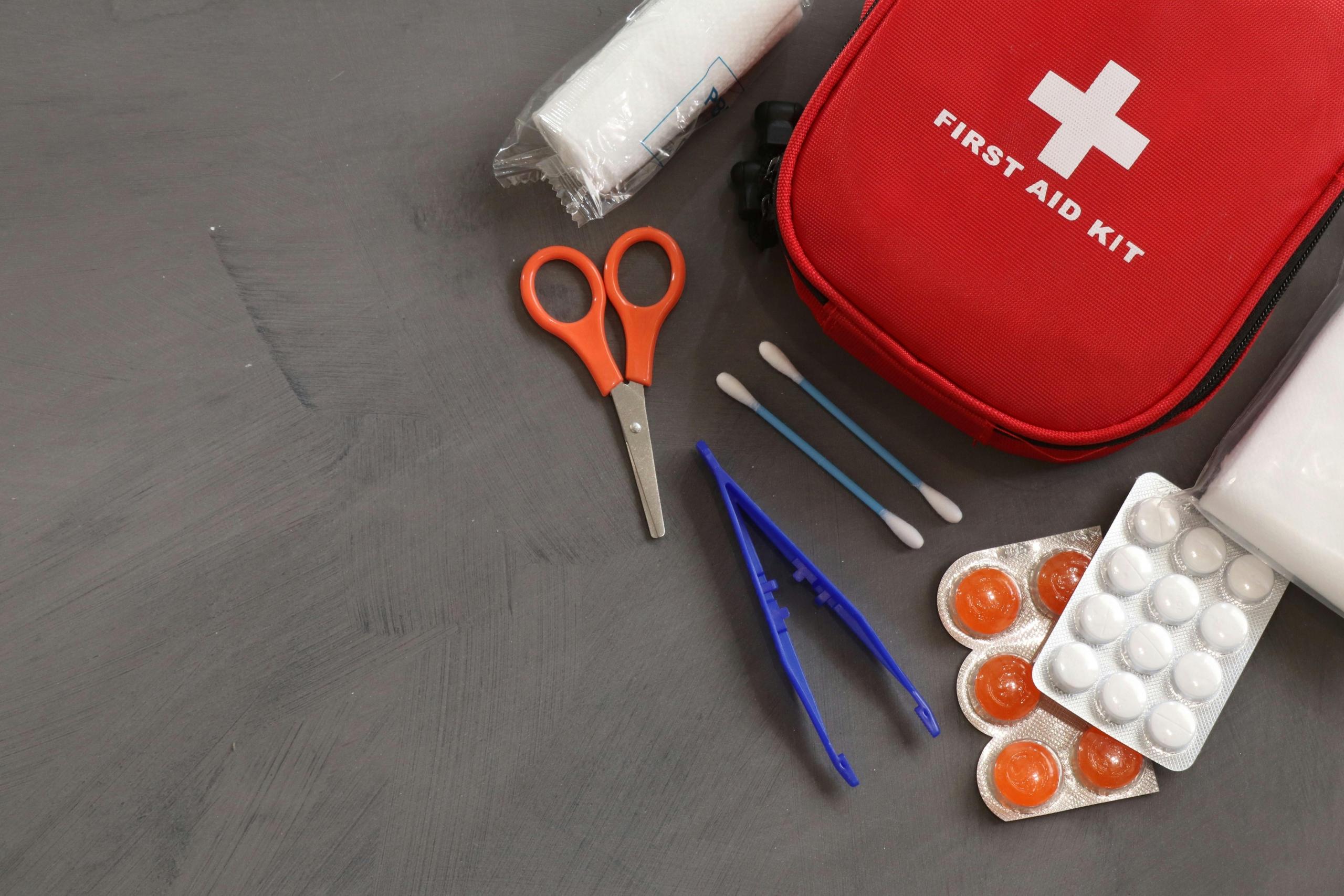 pills, scissors, tweezers and gauze placed alongside red first aid pouch