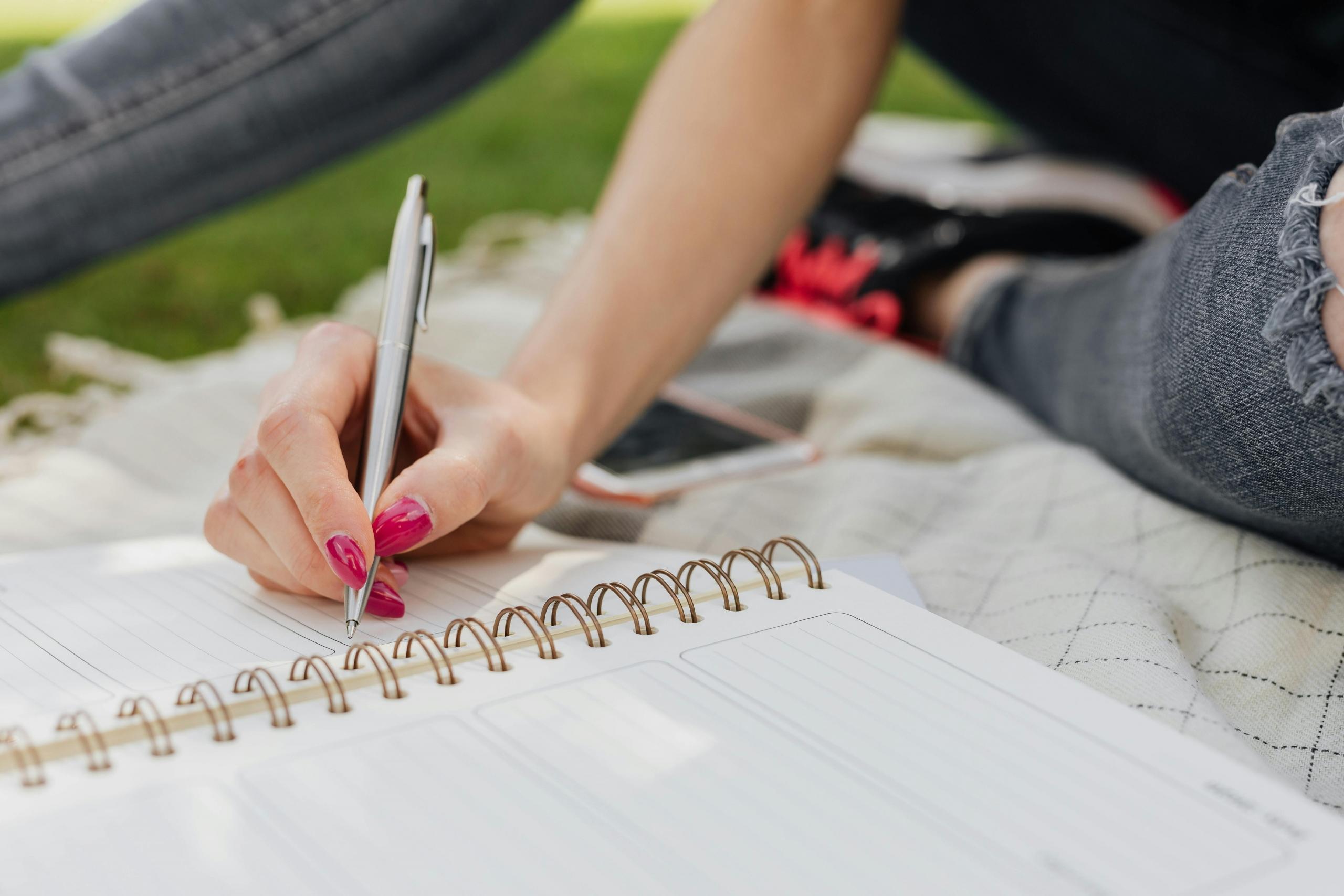 girl sitting on blanket on the grass writing in planner