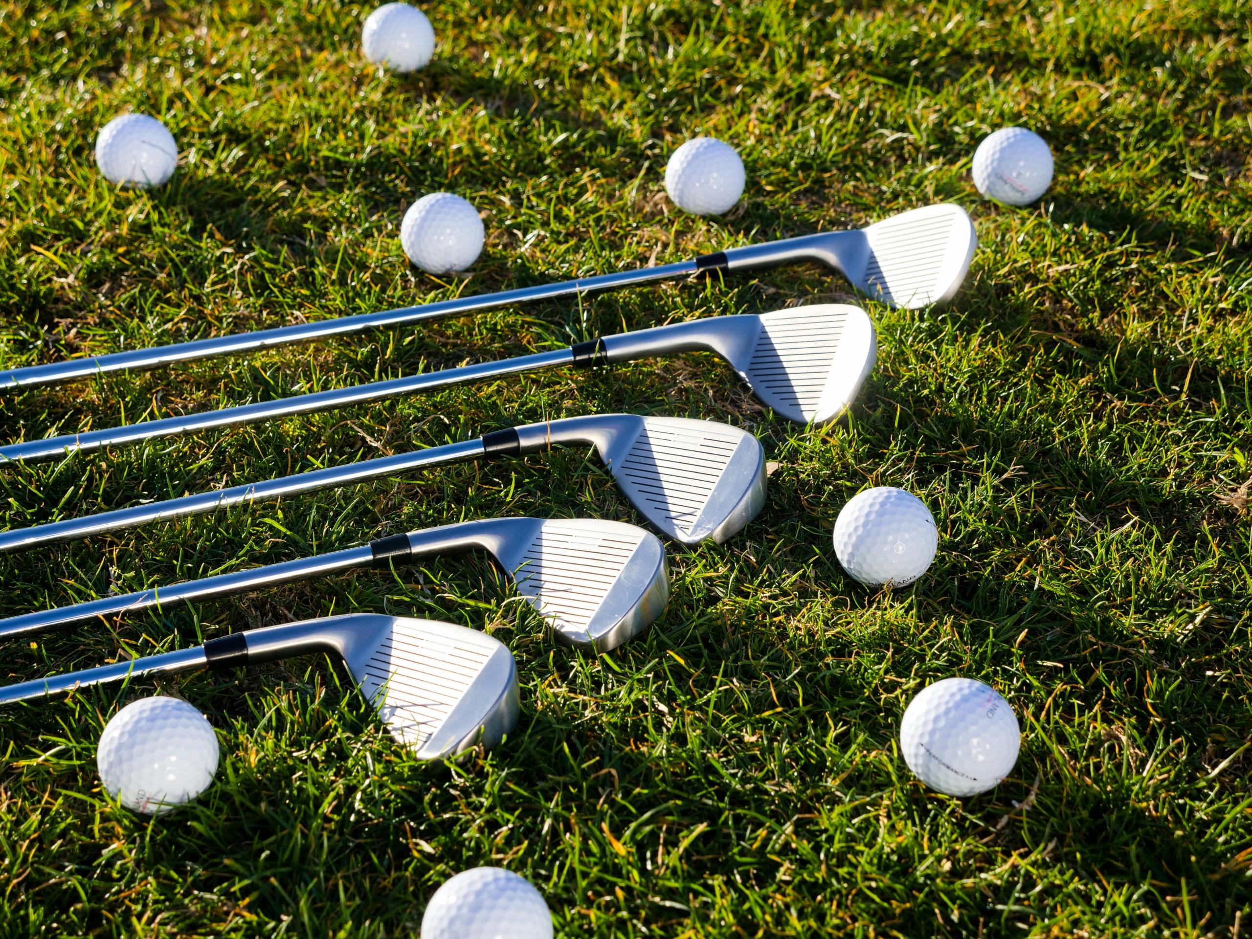 five golf clubs lying on the grass with golf balls scattered around them