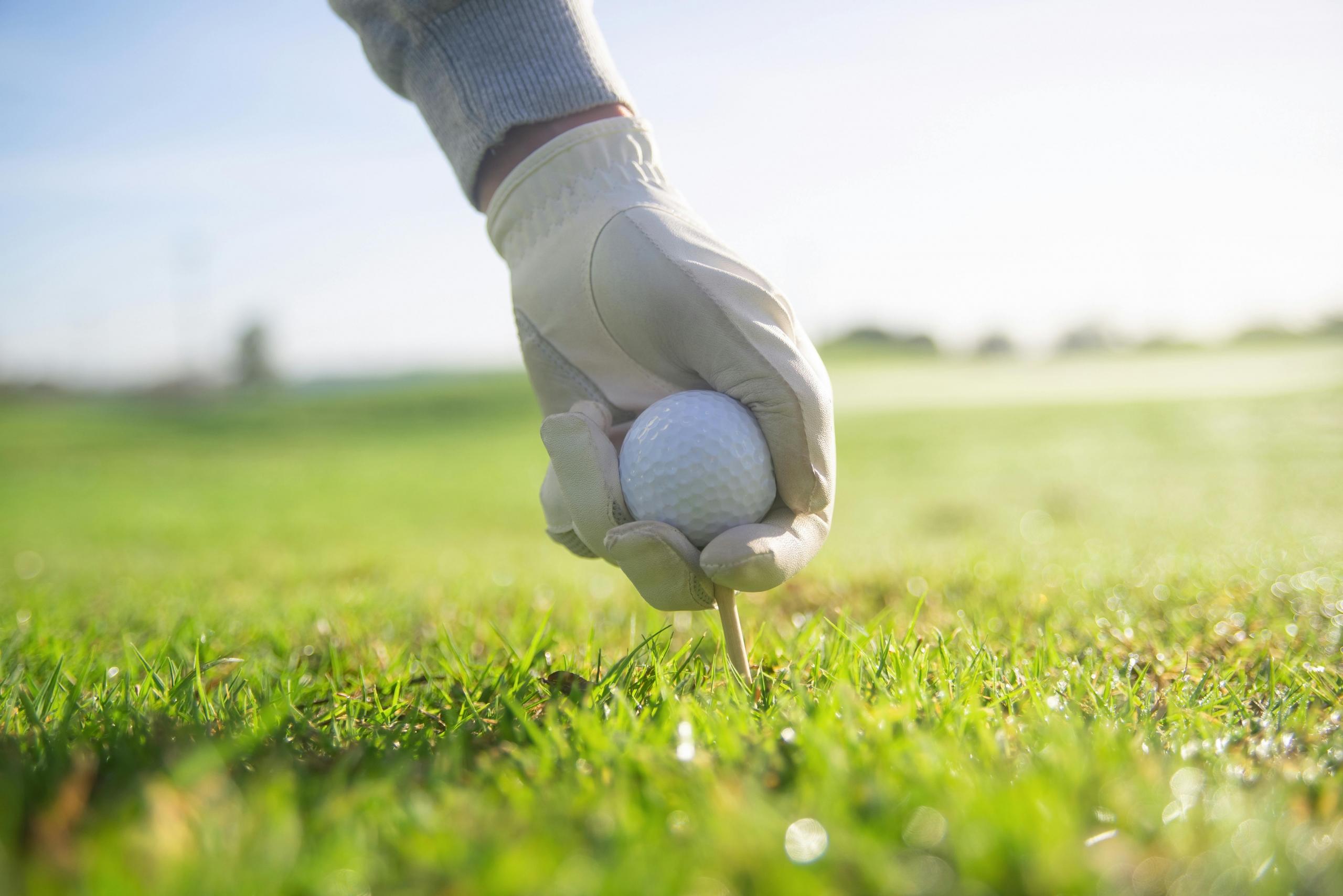 person placing golf tee and golf ball in the ground