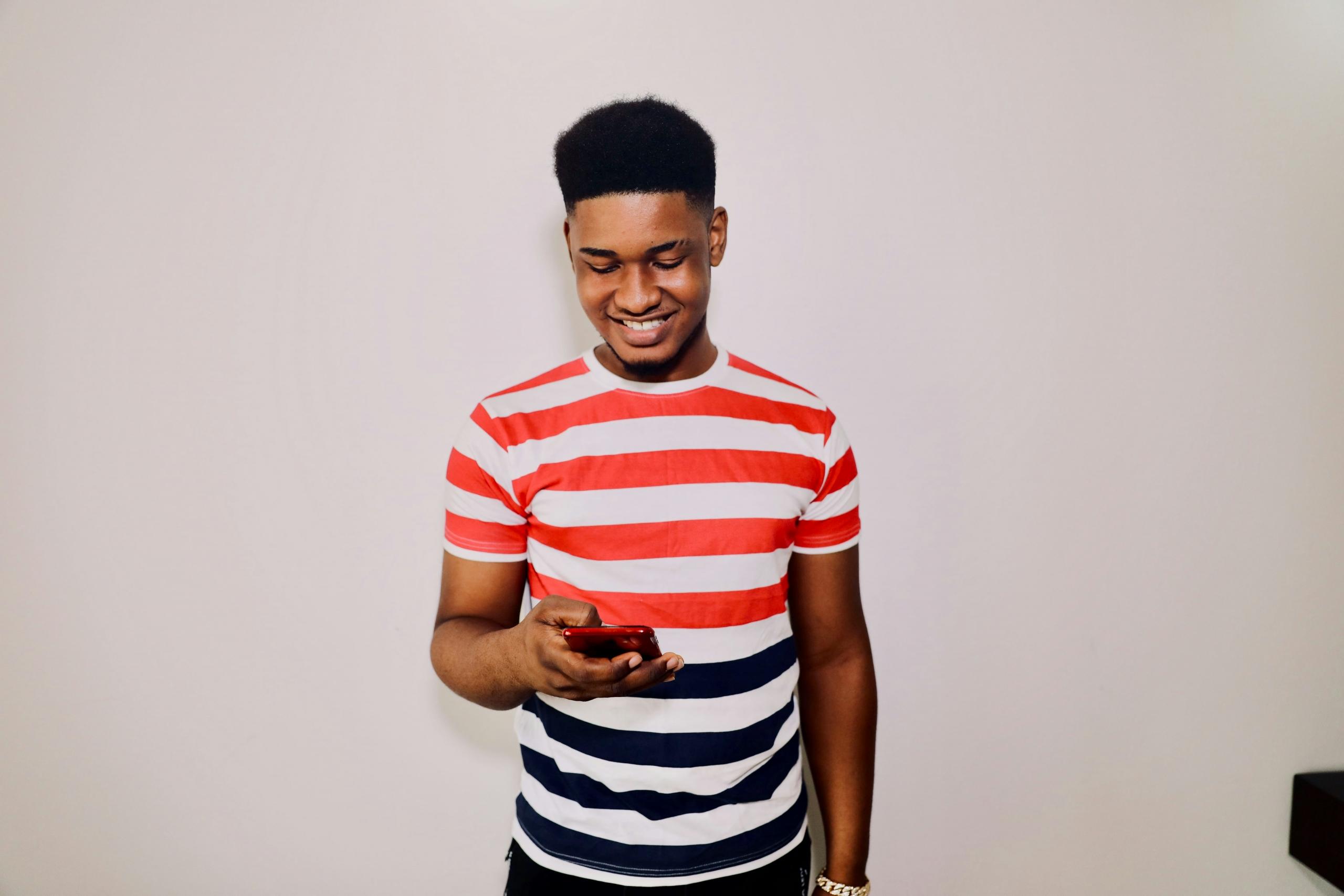 young adult in striped t-shirt smiling and using smartphone