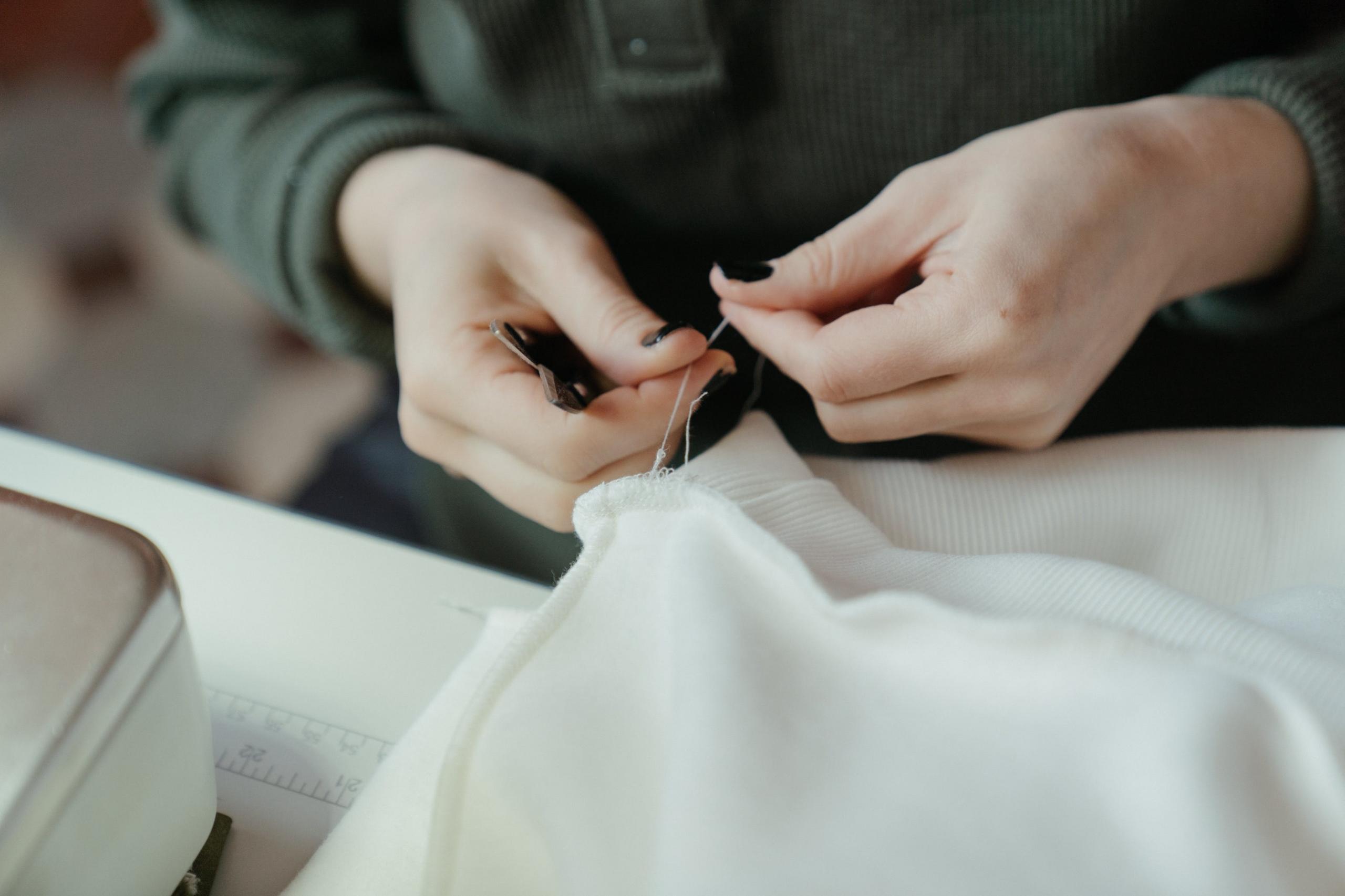 seamstress stitching garment with sewing machine and using scissors to cut threads