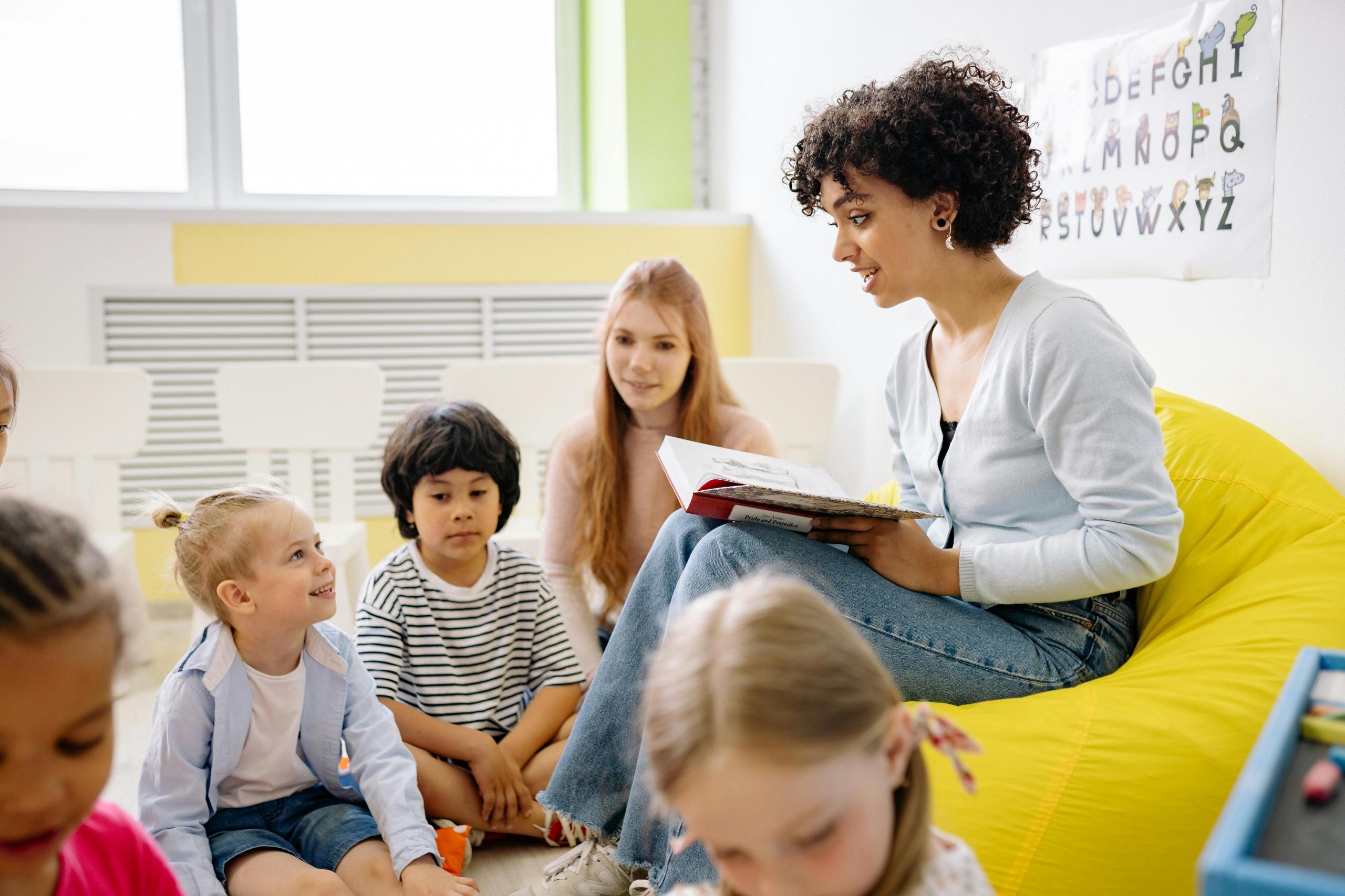 pre-school learners gathered around teacher as she reads a story to them
